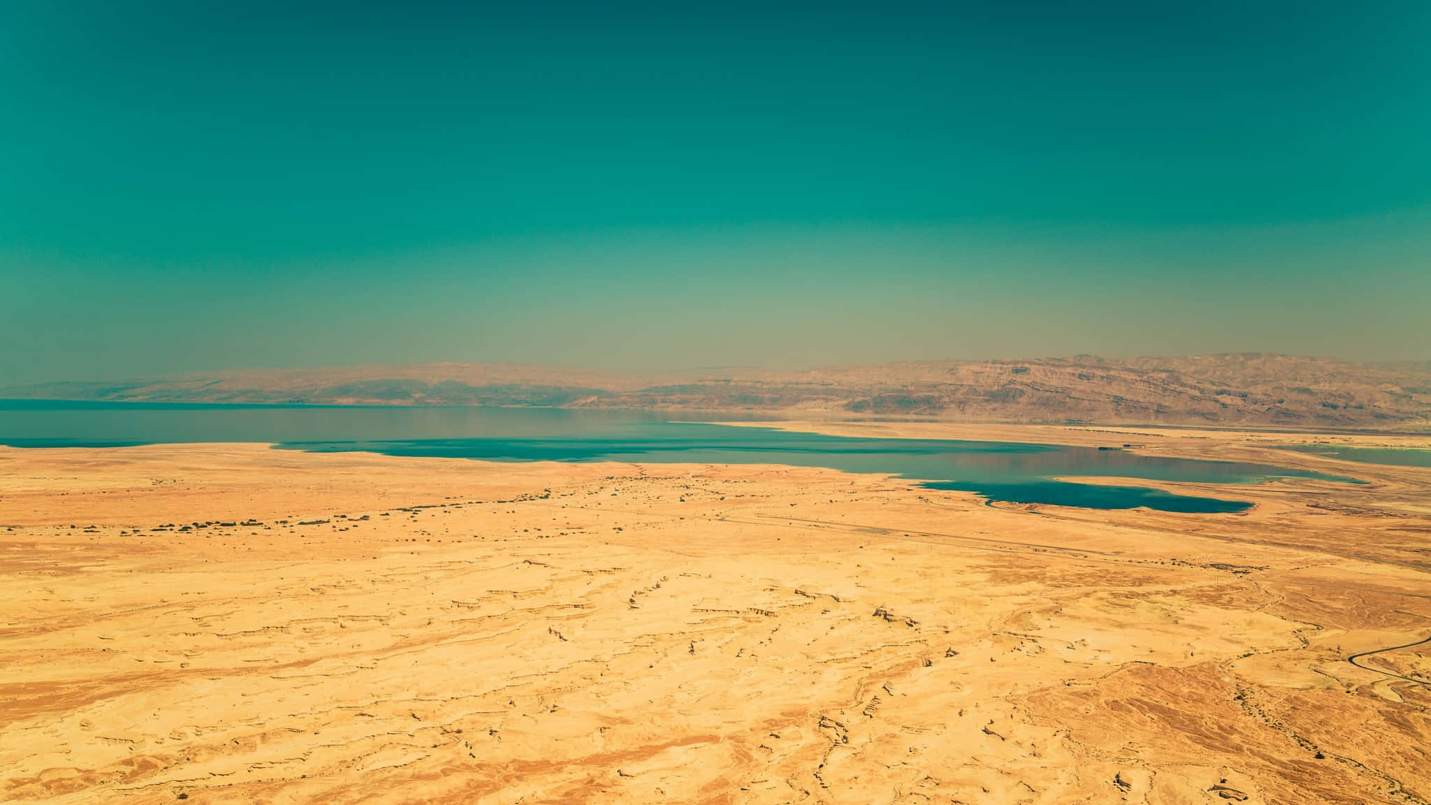 Israel 桌布 壁紙 — 廣闊乾旱的沙漠延伸至深藍綠色的湖泊，上方是漸變的藍綠色天空。