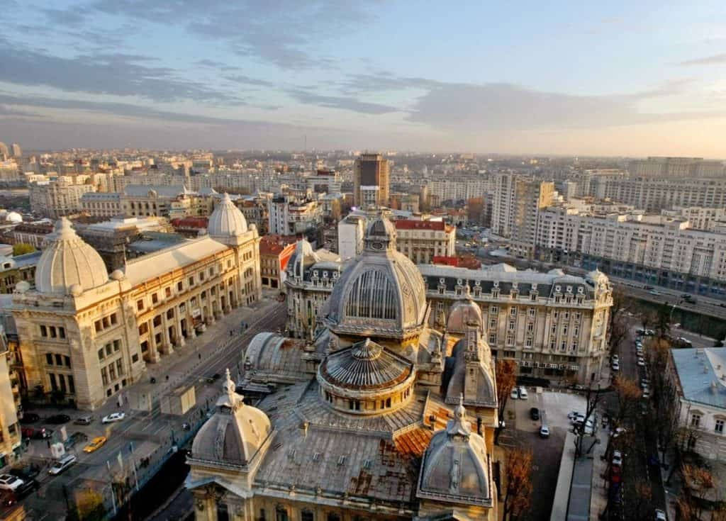 Romania 桌布 壁紙 — 廣闊城市景觀中宏偉圓頂建築的鳥瞰圖，沐浴在金色日落光芒中。