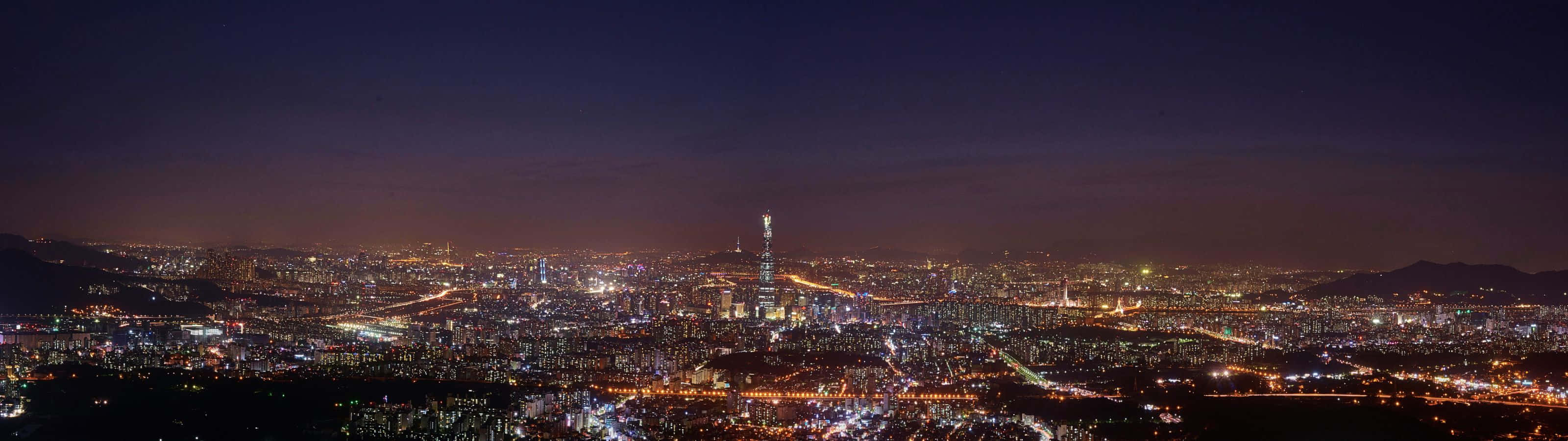 3200x900 桌布 壁紙 — 廣闊城市景觀的 panoramatic 夜景，無數燈光點亮，高塔在黑暗天空中突出。