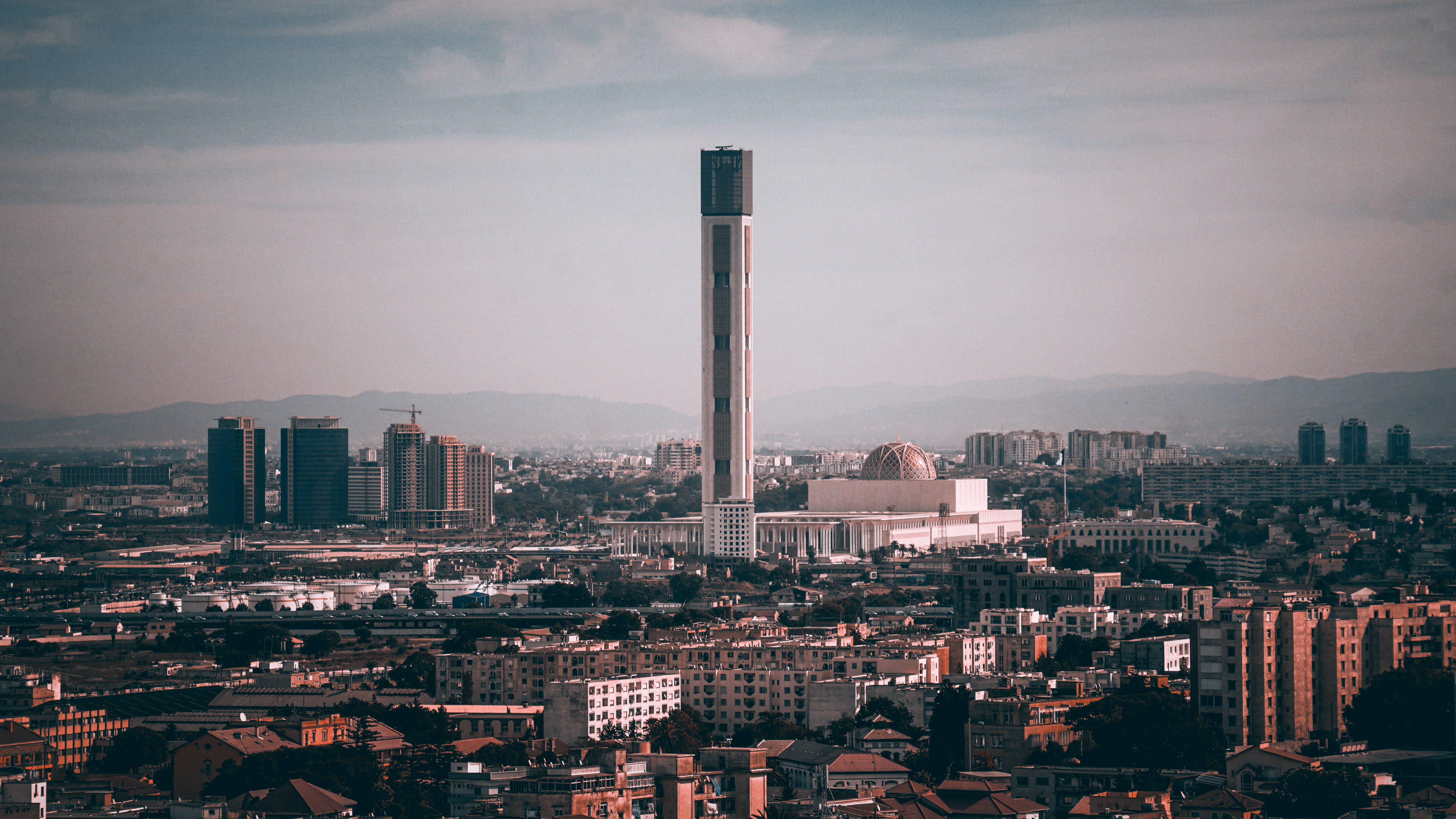 阿爾及利亞 桌布 壁紙 — 廣闊城市景觀的全景，以高聳的現代塔樓和圓頂清真寺為主，天空朦朧。
