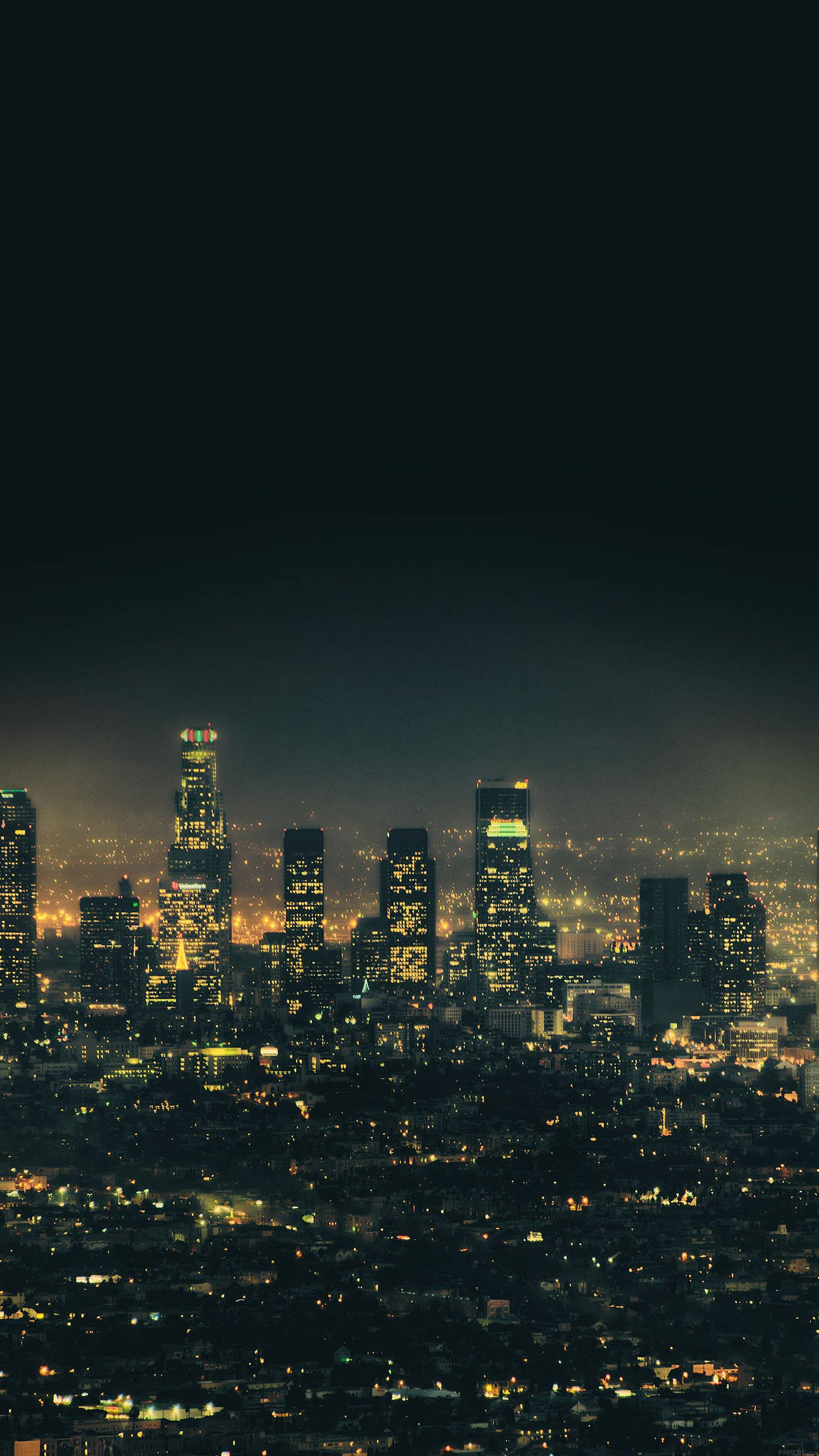 Smartphone 桌布 壁紙 — 廣闊城市景觀的夜景全景，高聳的摩天大樓在黑暗的天空中閃爍著溫暖的黃色燈光。