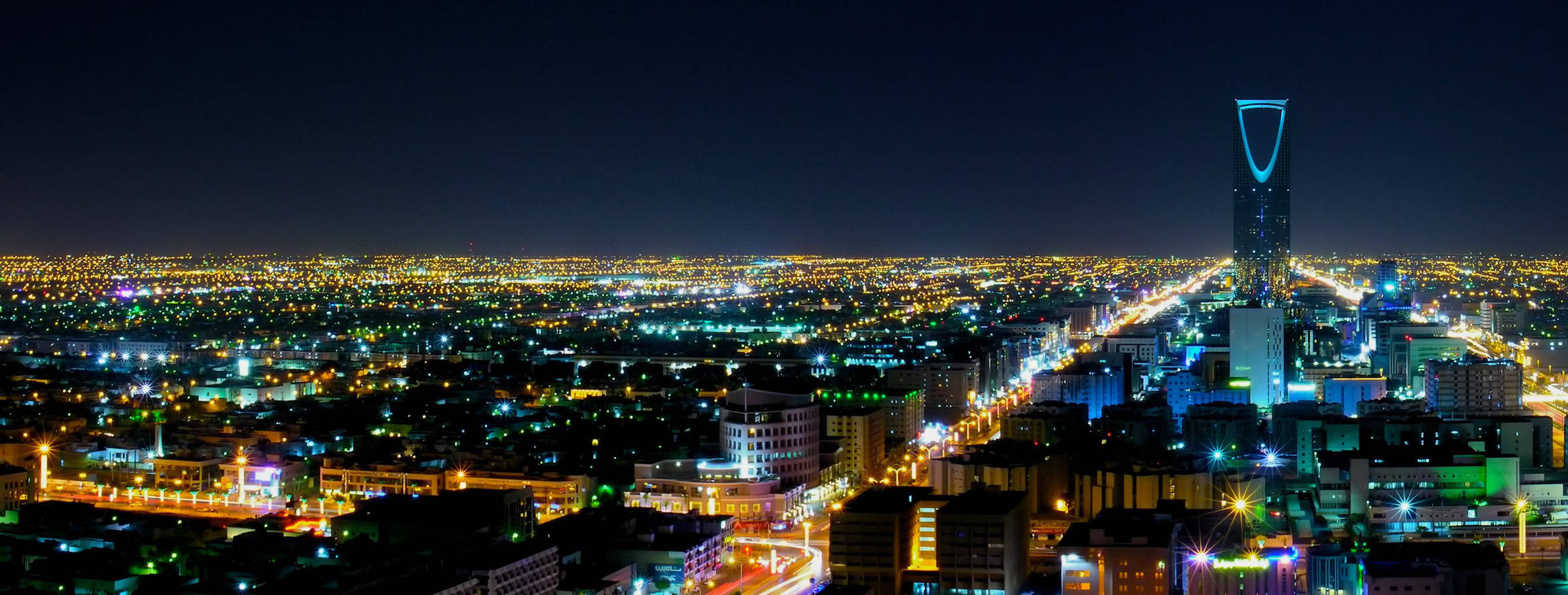 Riyadh 桌布 壁紙 — 廣闊城市景觀的夜間全景，無數燈光閃爍，以高聳的摩天大樓為中心。