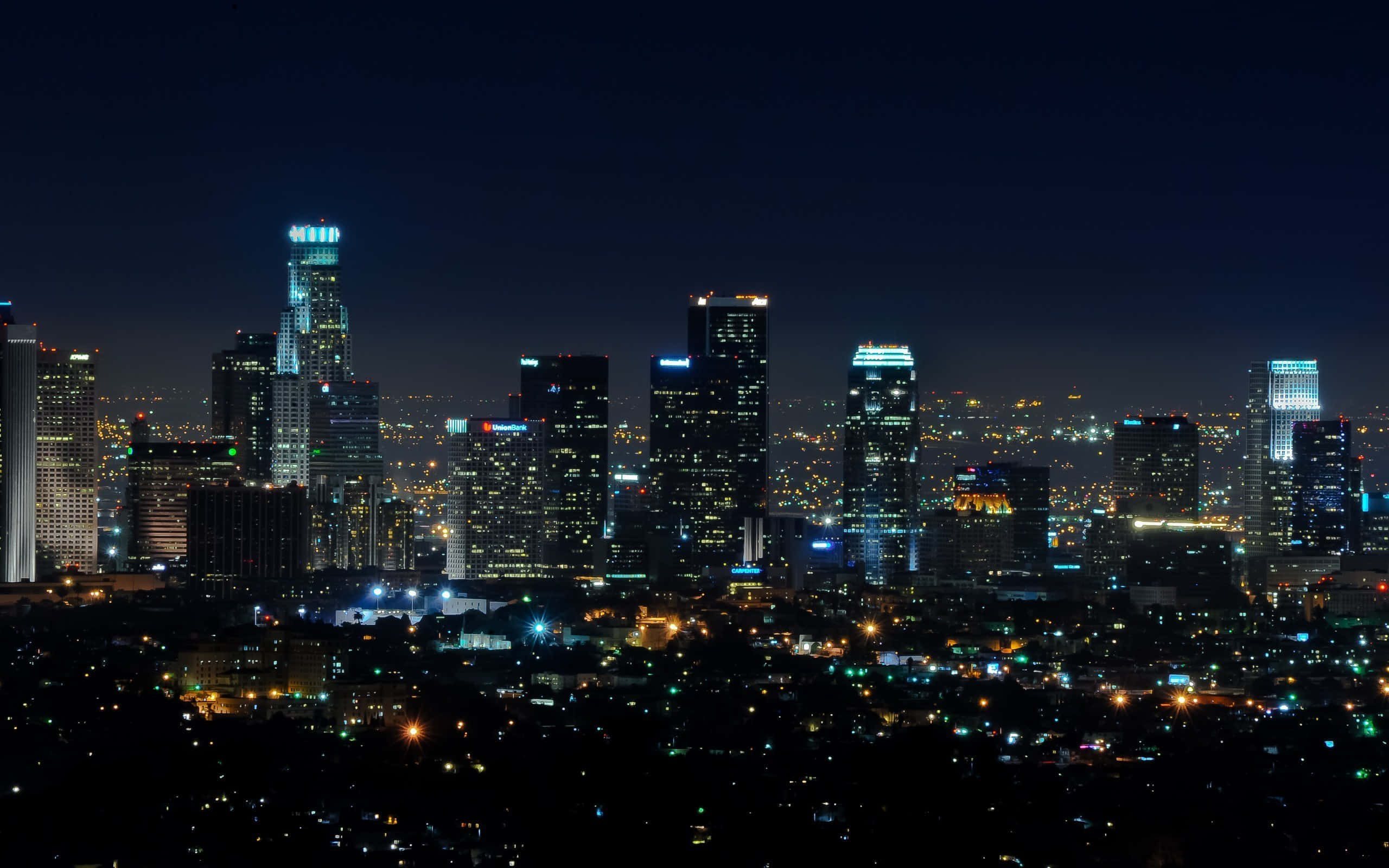 城市 桌布 壁紙 — 廣闊城市景觀的夜間全景，高聳的摩天大樓在黑暗的天空中閃耀。