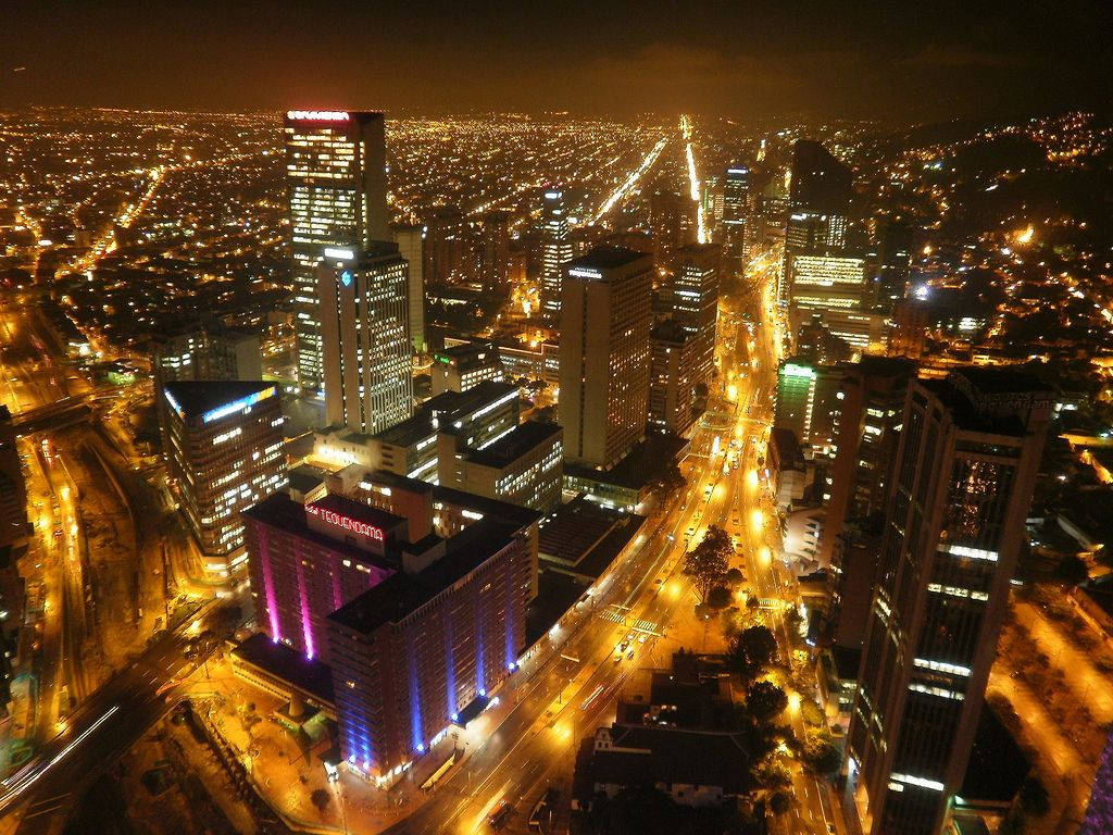 Bogota 桌布 壁紙 — 廣闊城市景觀的夜間空拍圖，閃爍的摩天大樓和燈火通明的街道延伸至遠方。