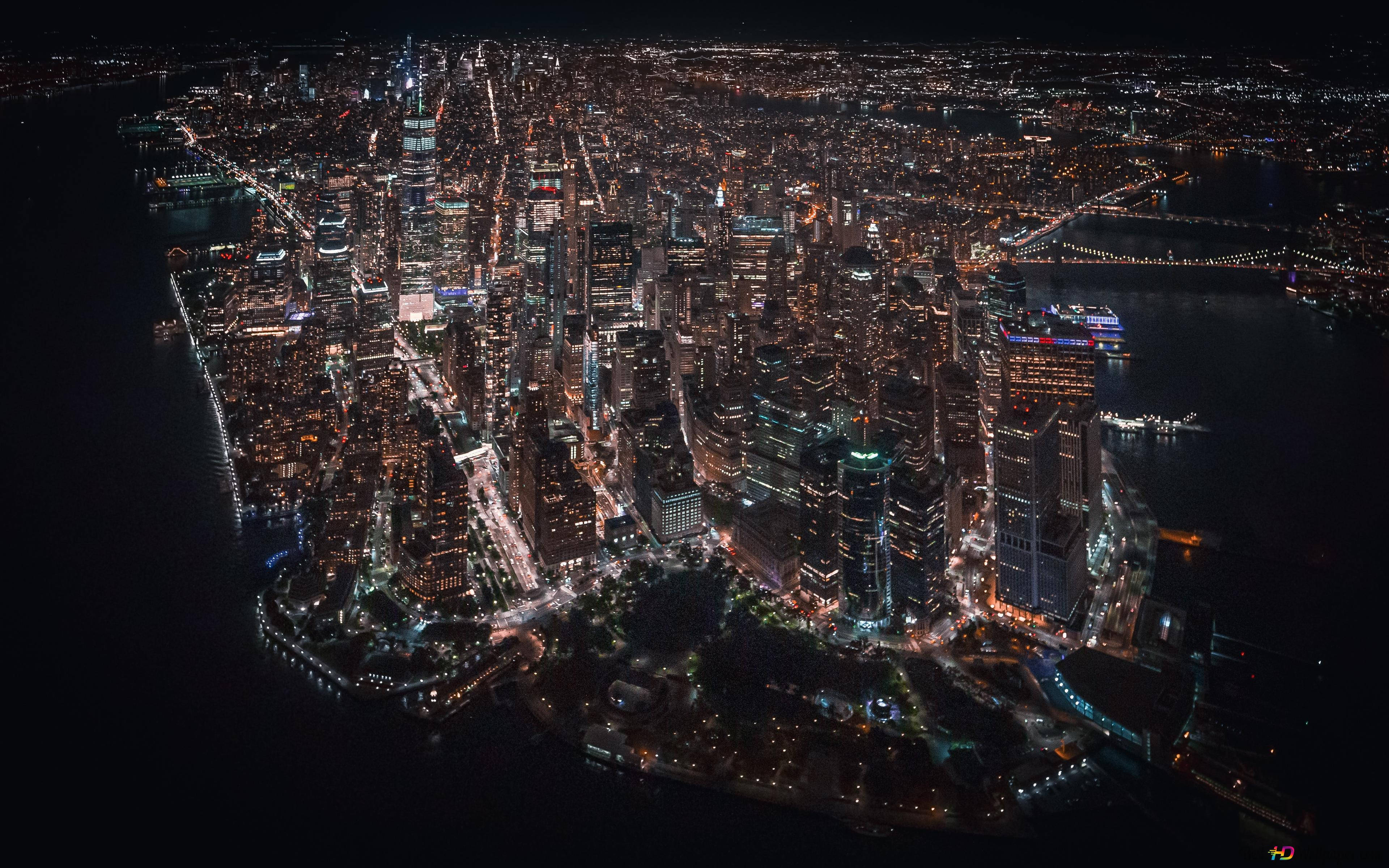 4K New York City 桌布 壁紙 — 廣闊城市景觀的夜間航拍，黑暗水面上有發光的摩天大樓和燈火通明的橋樑。