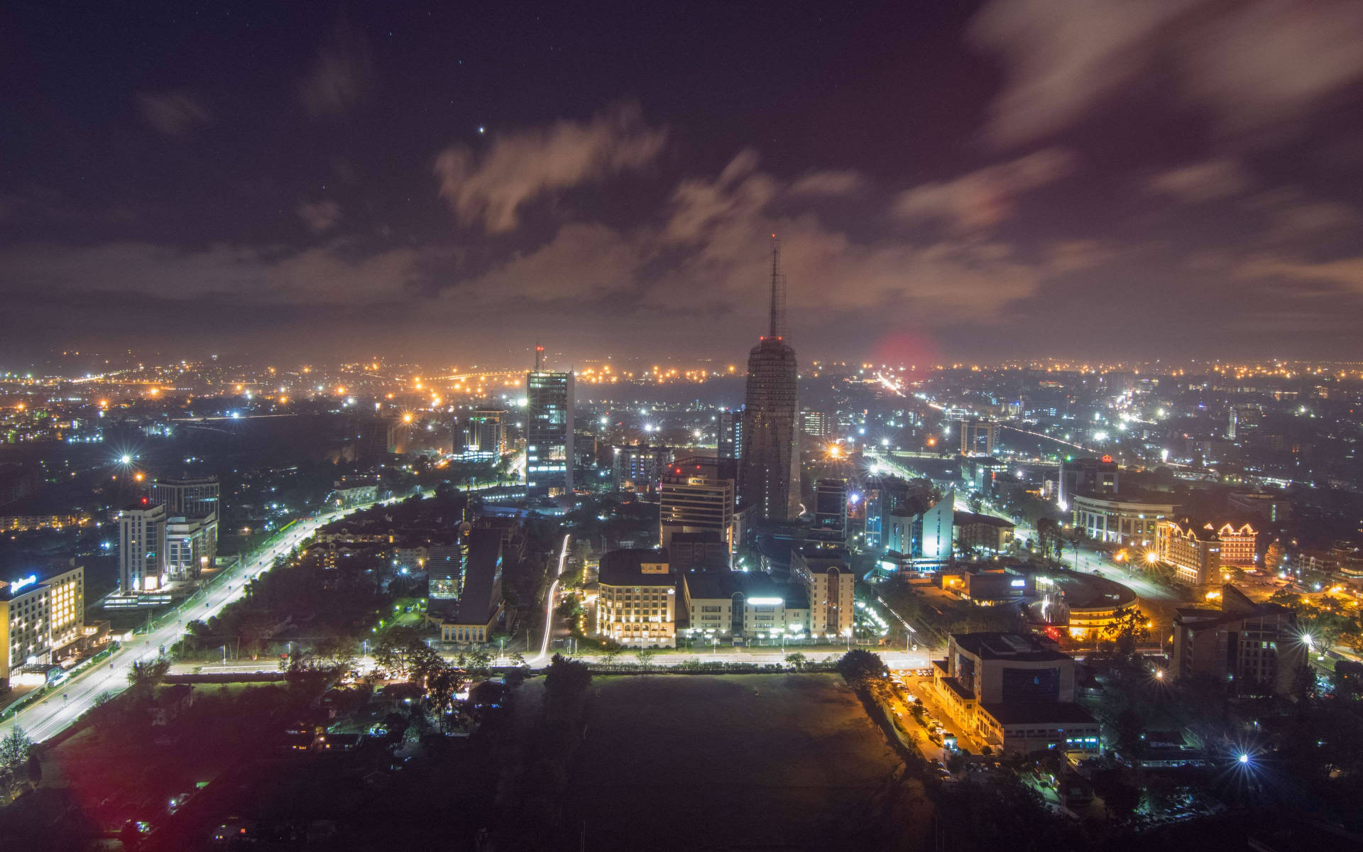 Africa 桌布 壁紙 — 廣闊城市景觀的夜間航拍圖，無數燈光在星空和飄動的雲層下照亮。