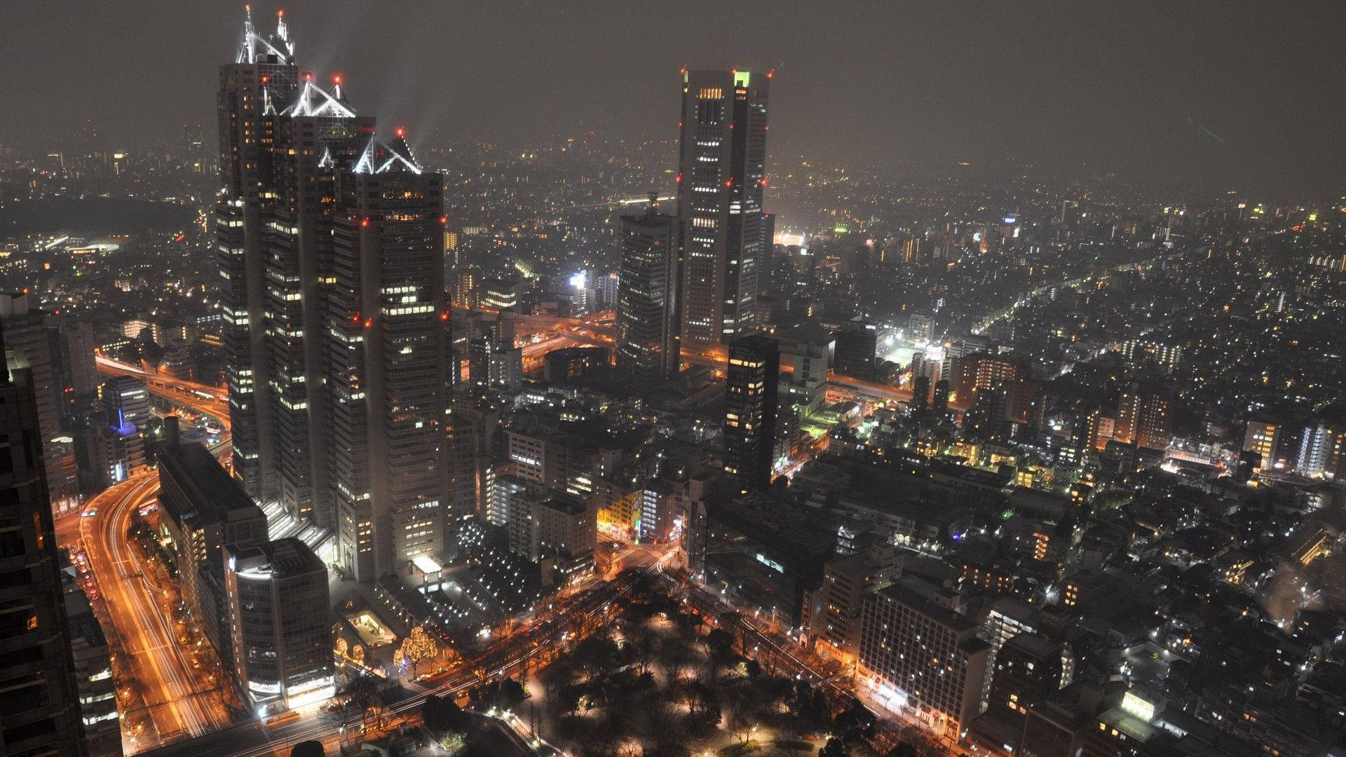 日本 桌布 壁紙 — 廣闊城市景觀的夜間鳥瞰圖，高聳的摩天大樓和下方發光的街道。