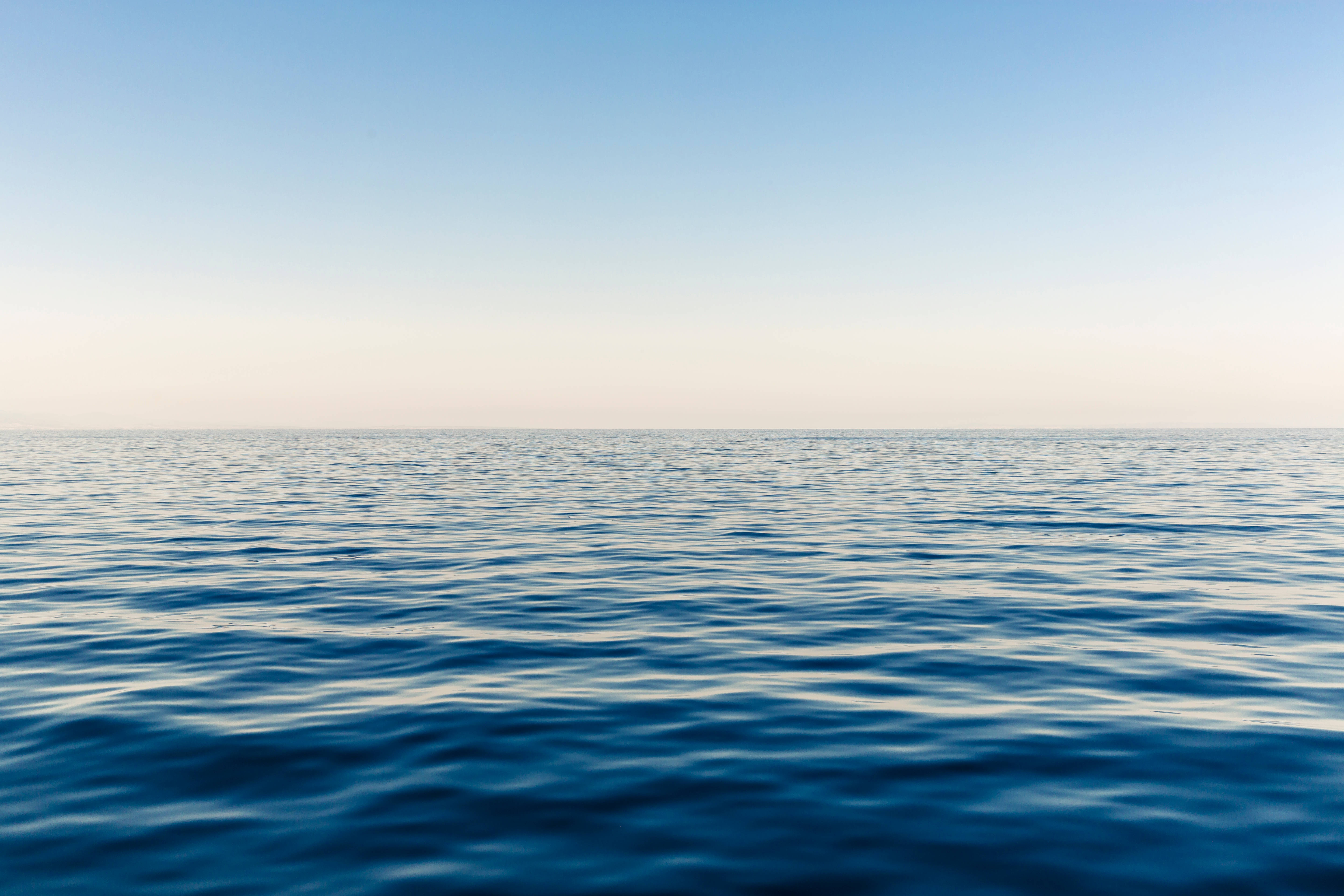 海洋 桌布 壁紙 — 廣闊平靜的海洋在柔和漸變的天空下延伸至地平線，寧靜的黎明。