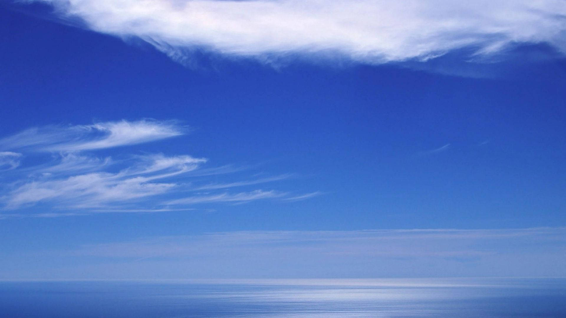 View 桌布 壁紙 — 廣闊平靜的海洋在柔和縷縷雲朵下與無盡天空相遇，呈現寧靜的日光。