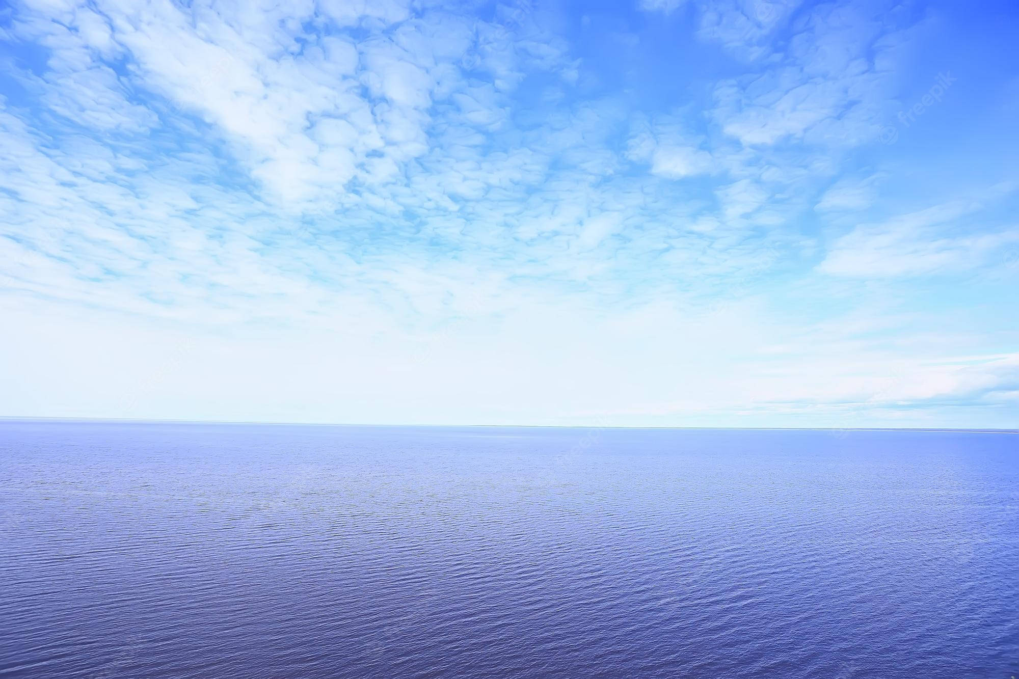 海洋 桌布 壁紙 — 廣闊平靜的海洋在柔和縹緲的雲朵下與天空相遇，沐浴在寧靜的日光中。