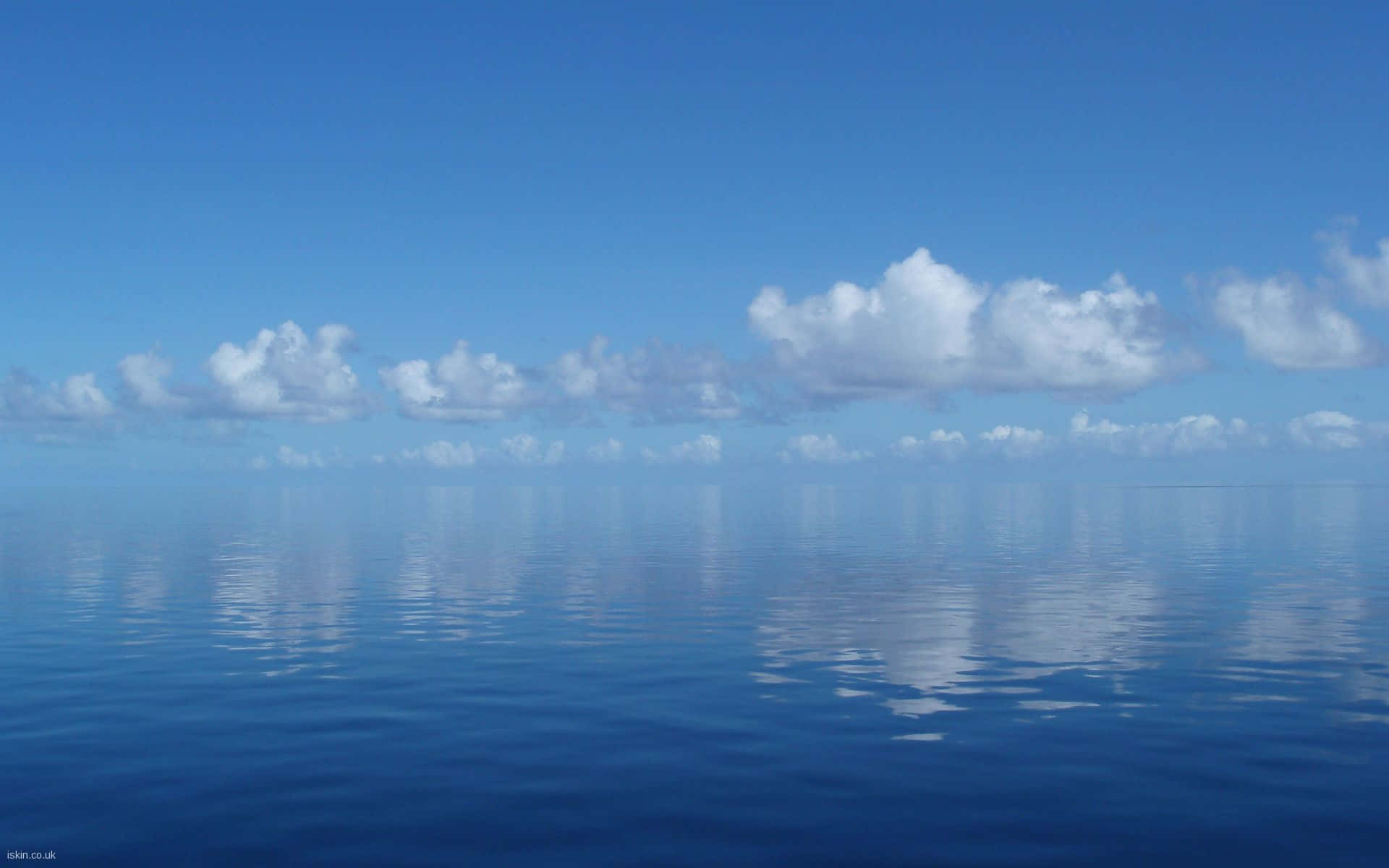 Soothing 桌布 壁紙 — 廣闊平靜的海洋在清澈的藍天下映照著蓬鬆的白雲，營造出寧靜的對稱。
