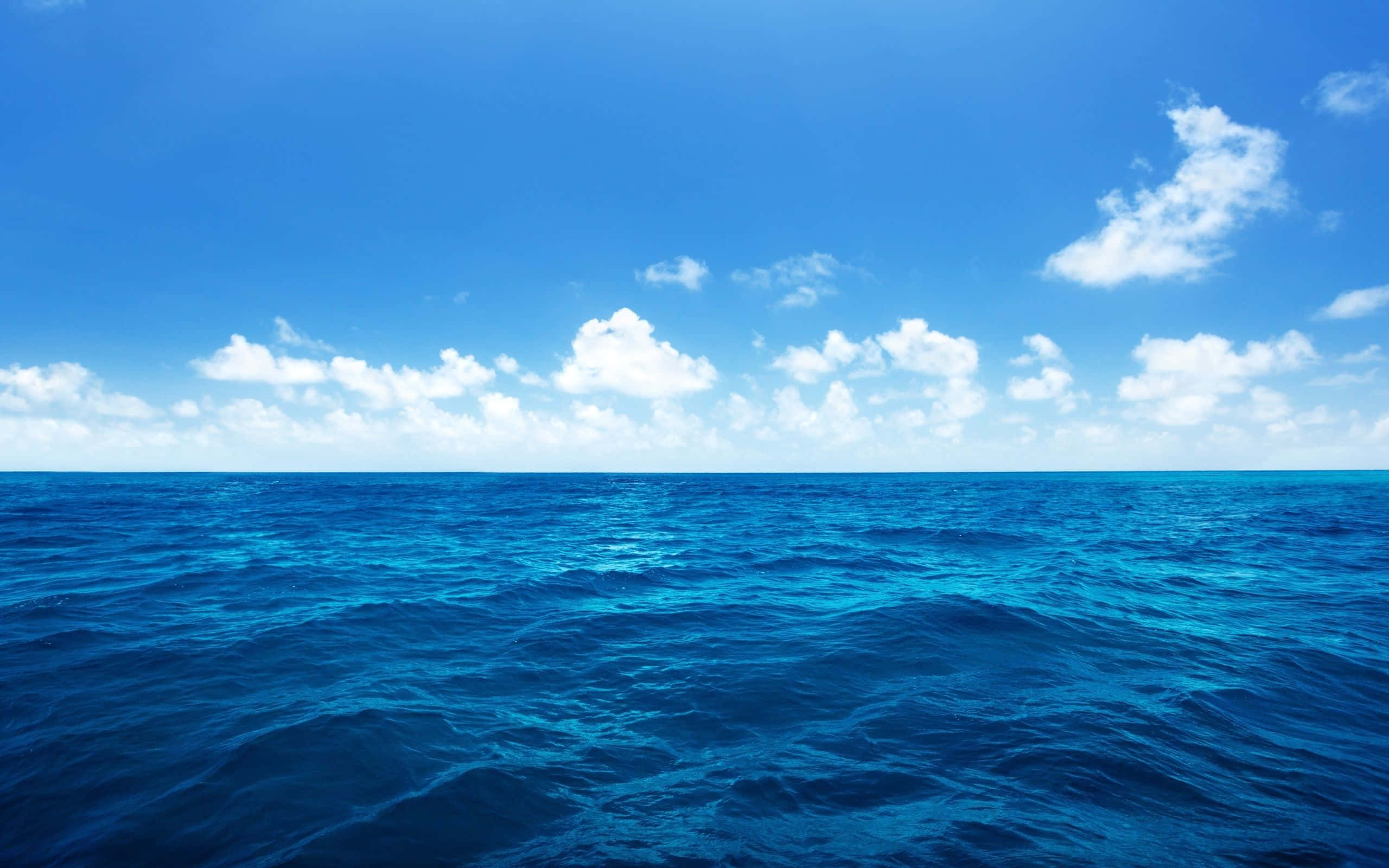 水 桌布 壁紙 — 廣闊深藍海洋波浪在明亮天空下泛起漣漪，天空點綴著蓬鬆白雲。