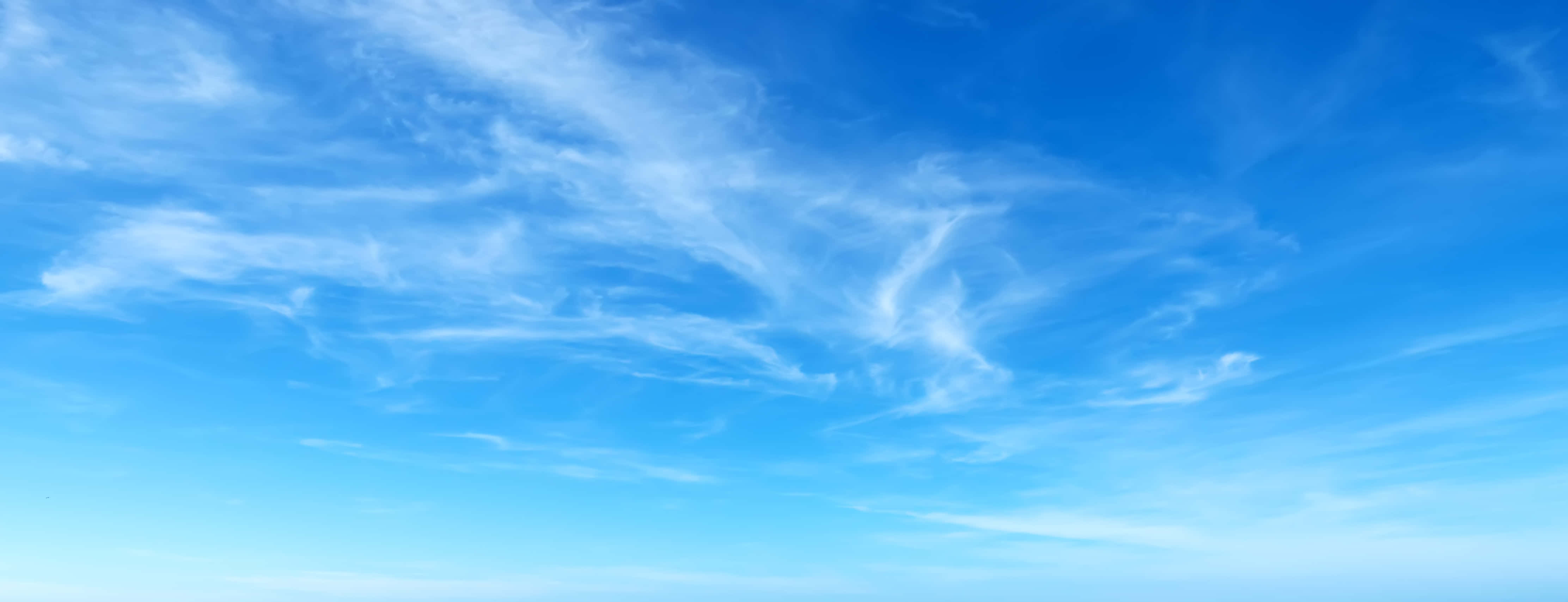 Blue Skies 桌布 壁紙 — 廣闊清澈的藍天，縷縷白雲在寧靜的地平線上飄移。