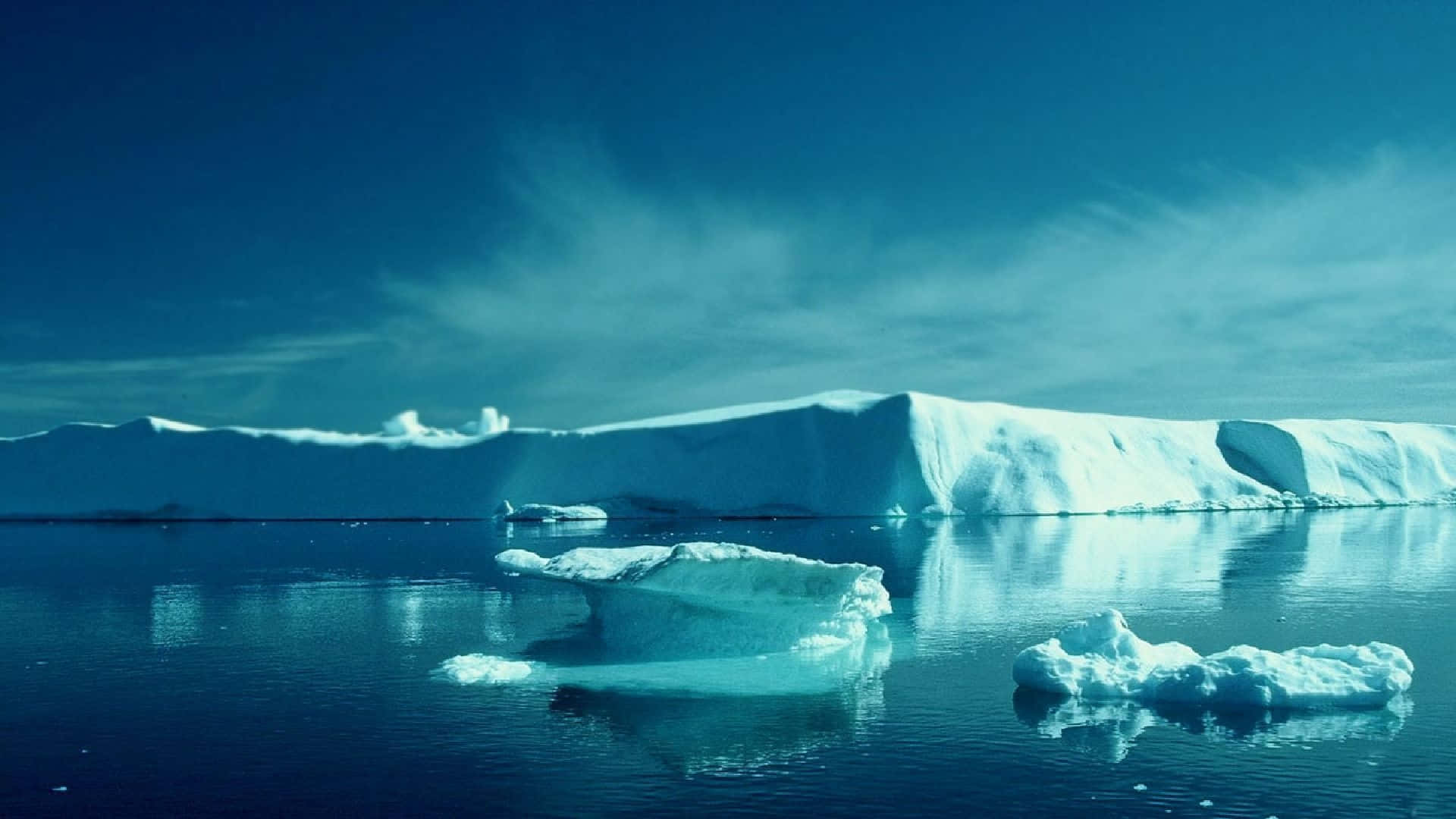 North Pole 桌布 壁紙 — 廣闊的冰河聳立在平靜的藍色水域上，漂浮的冰山在晴朗的天空下反射。