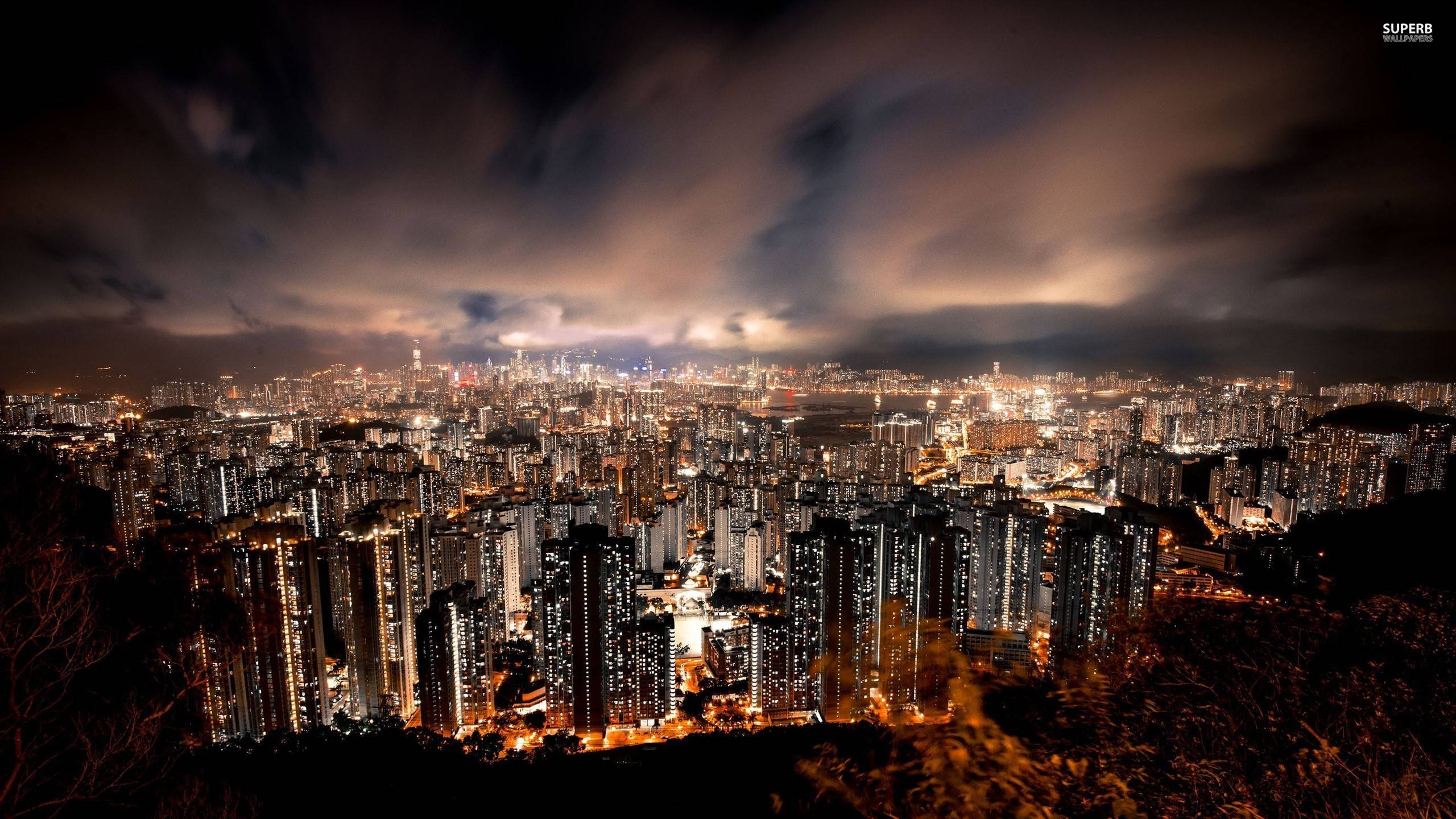 城市風景 桌布 壁紙 — 廣闊的城市夜景，無數燈火通明的摩天大樓在戲劇性的多雲天空下。