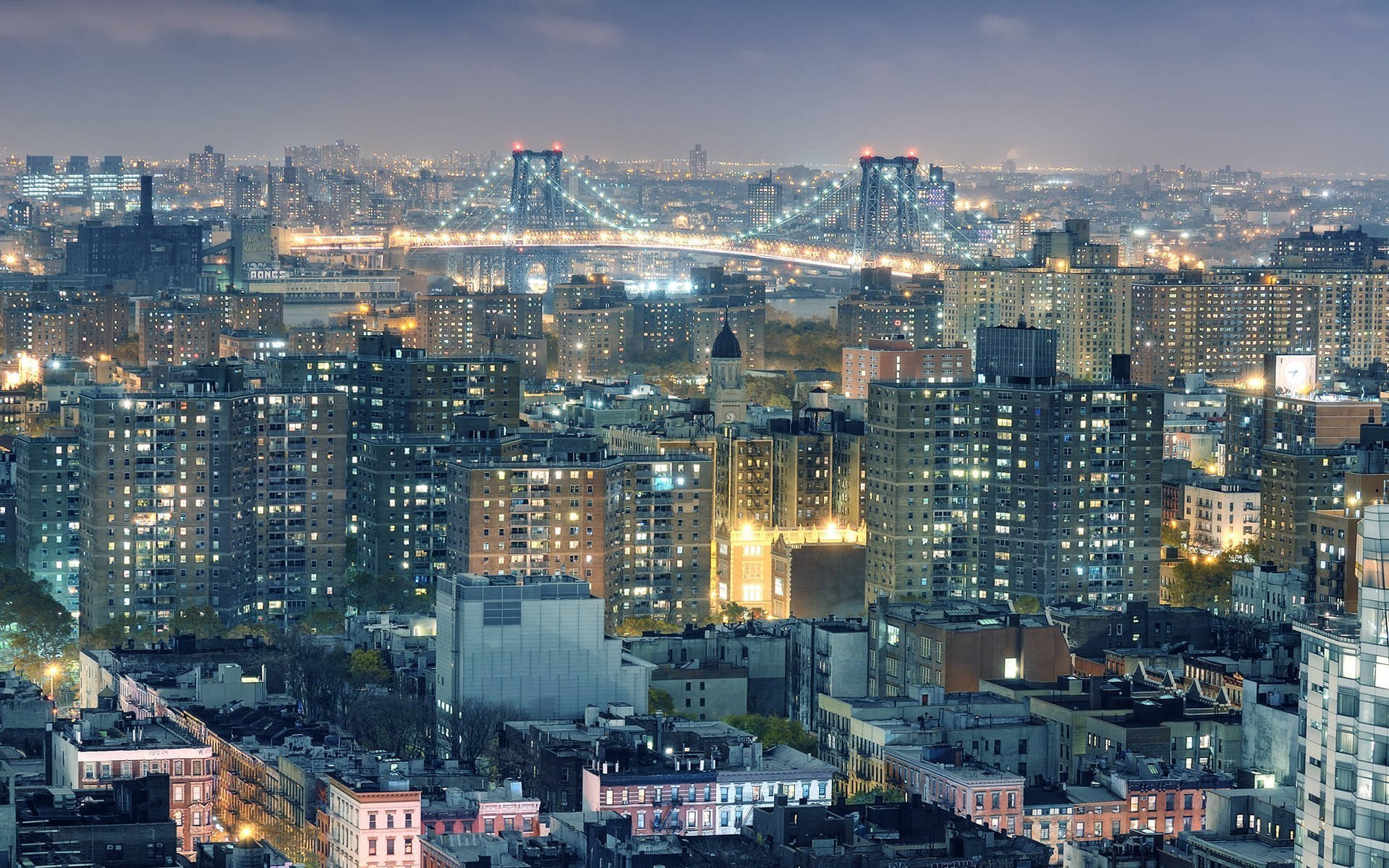New 桌布 壁紙 — 廣闊的城市夜景，閃爍的摩天大樓和一座在昏暗天空下橫跨河流的燈光橋樑。