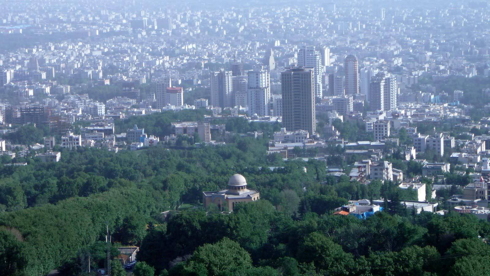 Tehran 桌布 壁紙 — 廣闊的城市天際線，密集的高層建築和低層建築坐落在茂密的綠樹之間，天空朦朧。
