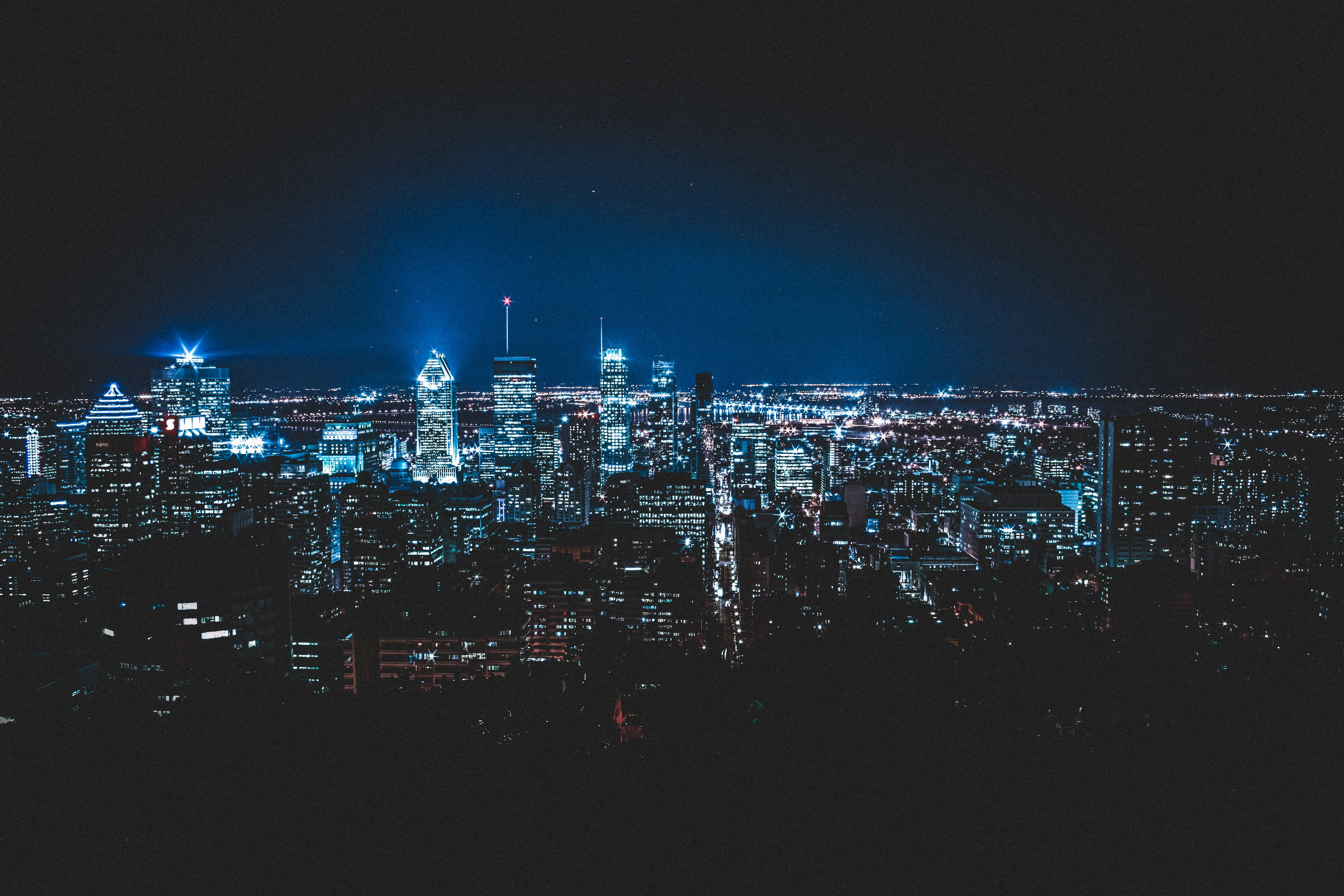 Montreal 桌布 壁紙 — 廣闊的城市天際線在夜晚沐浴在冷藍色霓虹燈光下，映襯著黑暗的天空。