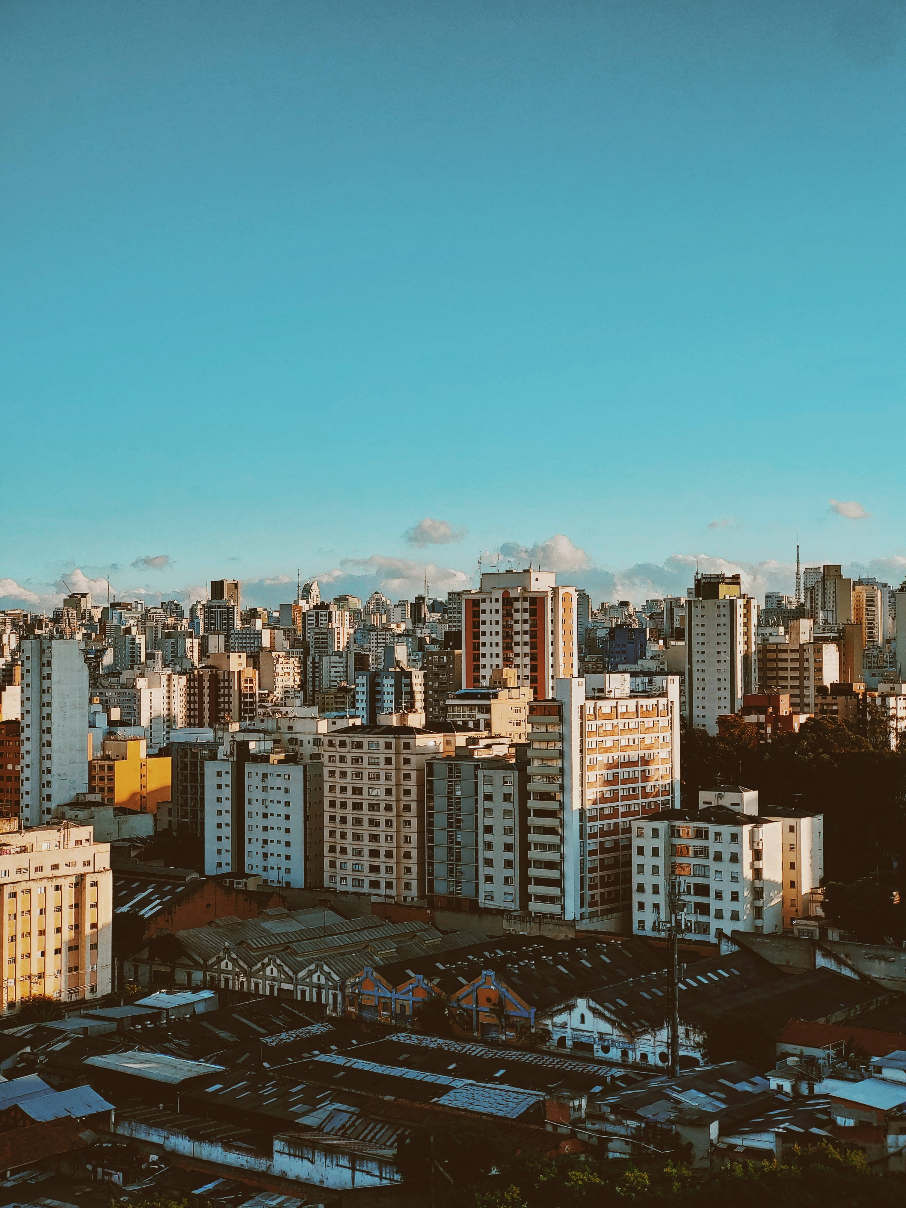 城市 桌布 壁紙 — 廣闊的城市天際線沐浴在金色的日落光芒中，高聳的建築物和清澈的藍天。