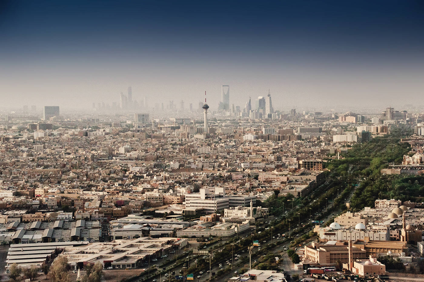 Riyadh 桌布 壁紙 — 廣闊的城市景觀，密集的低層建築逐漸消失在由現代摩天大樓和一座高聳的通訊塔主導的朦朧天際線中。