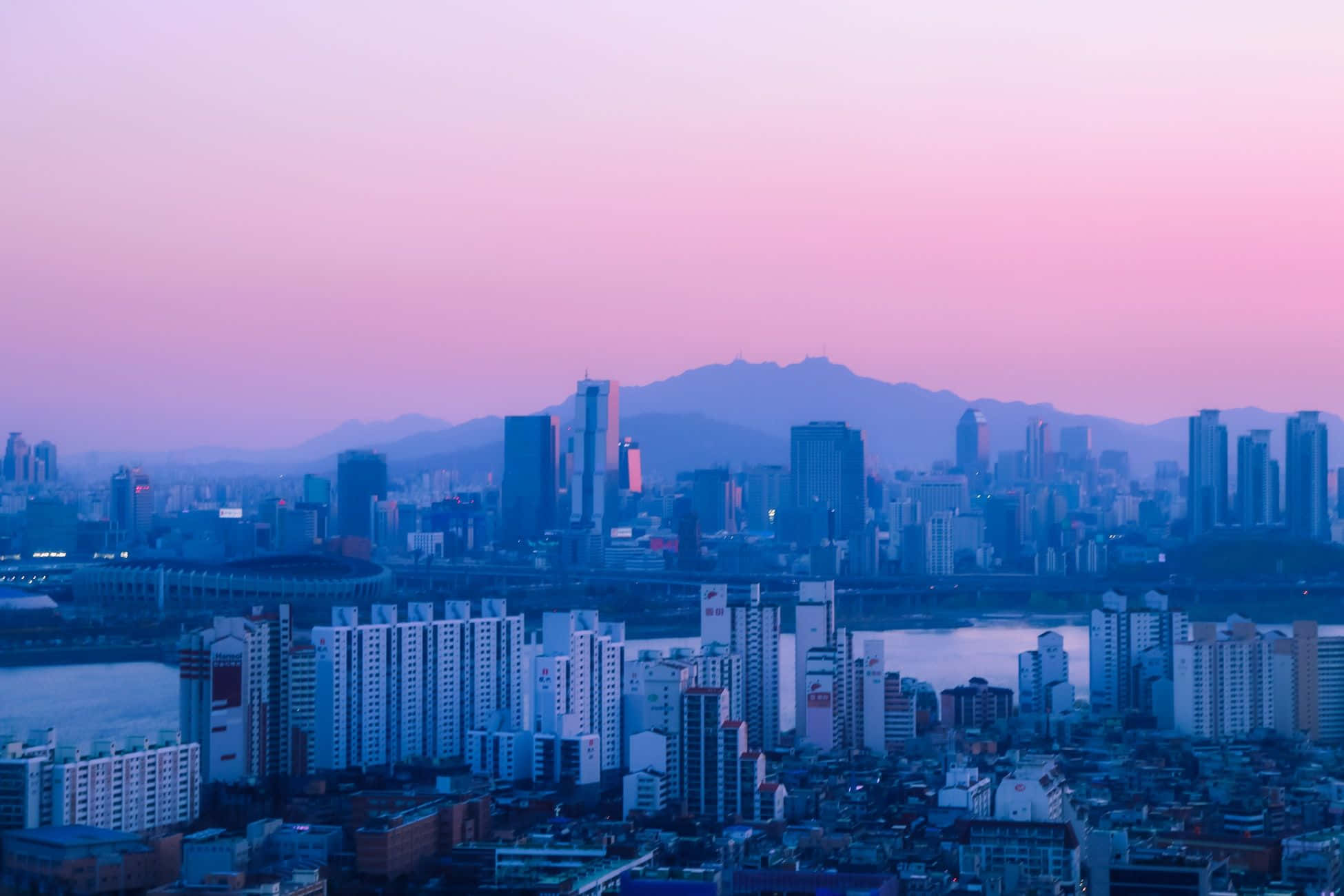 桌布 壁紙 — 廣闊的城市景觀沐浴在粉紅色和藍色的暮色中，遠山在天際線上形成剪影。