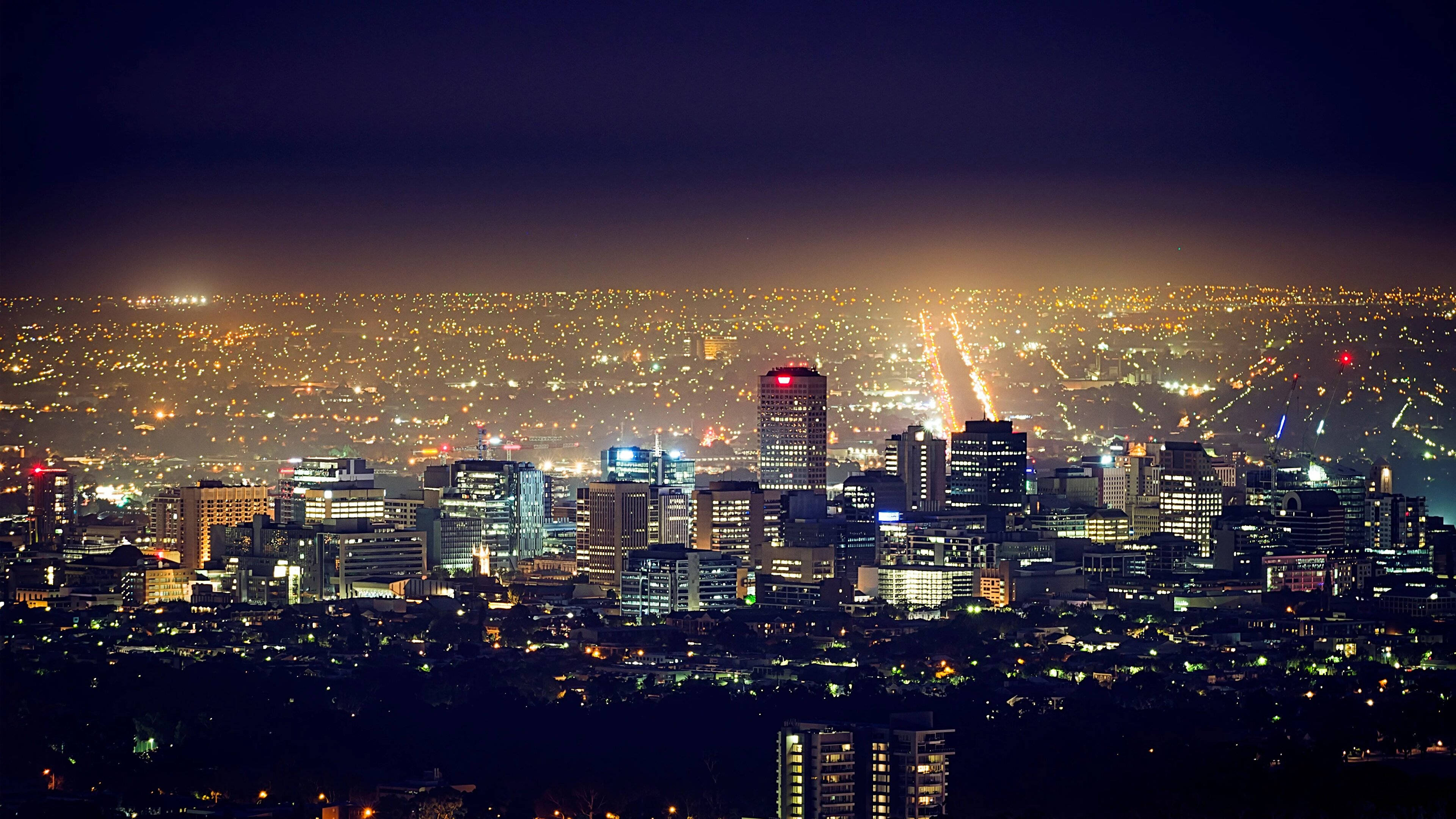Adelaide 桌布 壁紙 — 廣闊的夜景城市景觀，無數發光的燈光在黑暗的天空下照亮摩天大樓和街道。