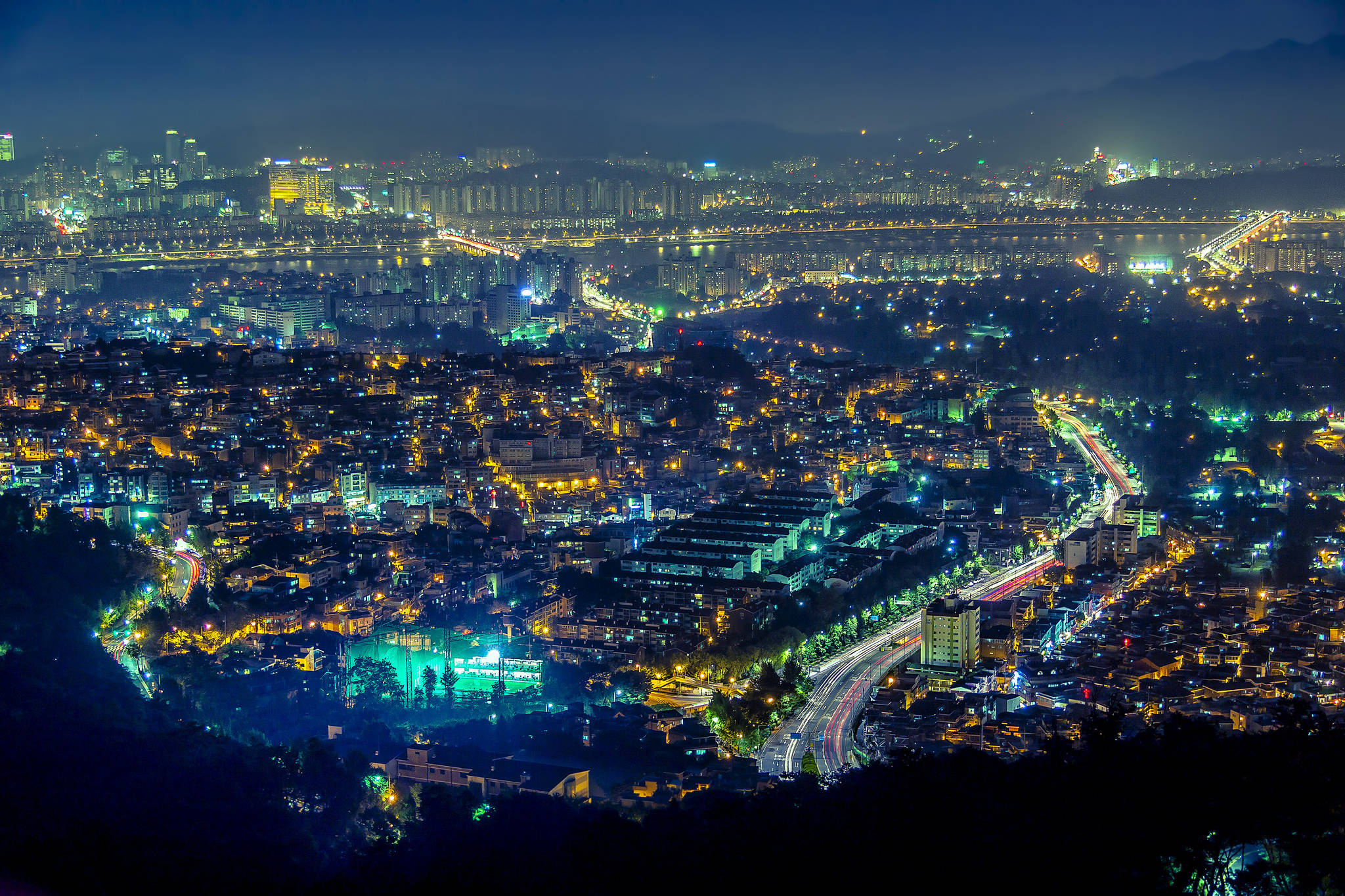 南韓 桌布 壁紙 — 廣闊的夜景城市景觀，發光的街道和建築物坐落於山丘和河流之間。