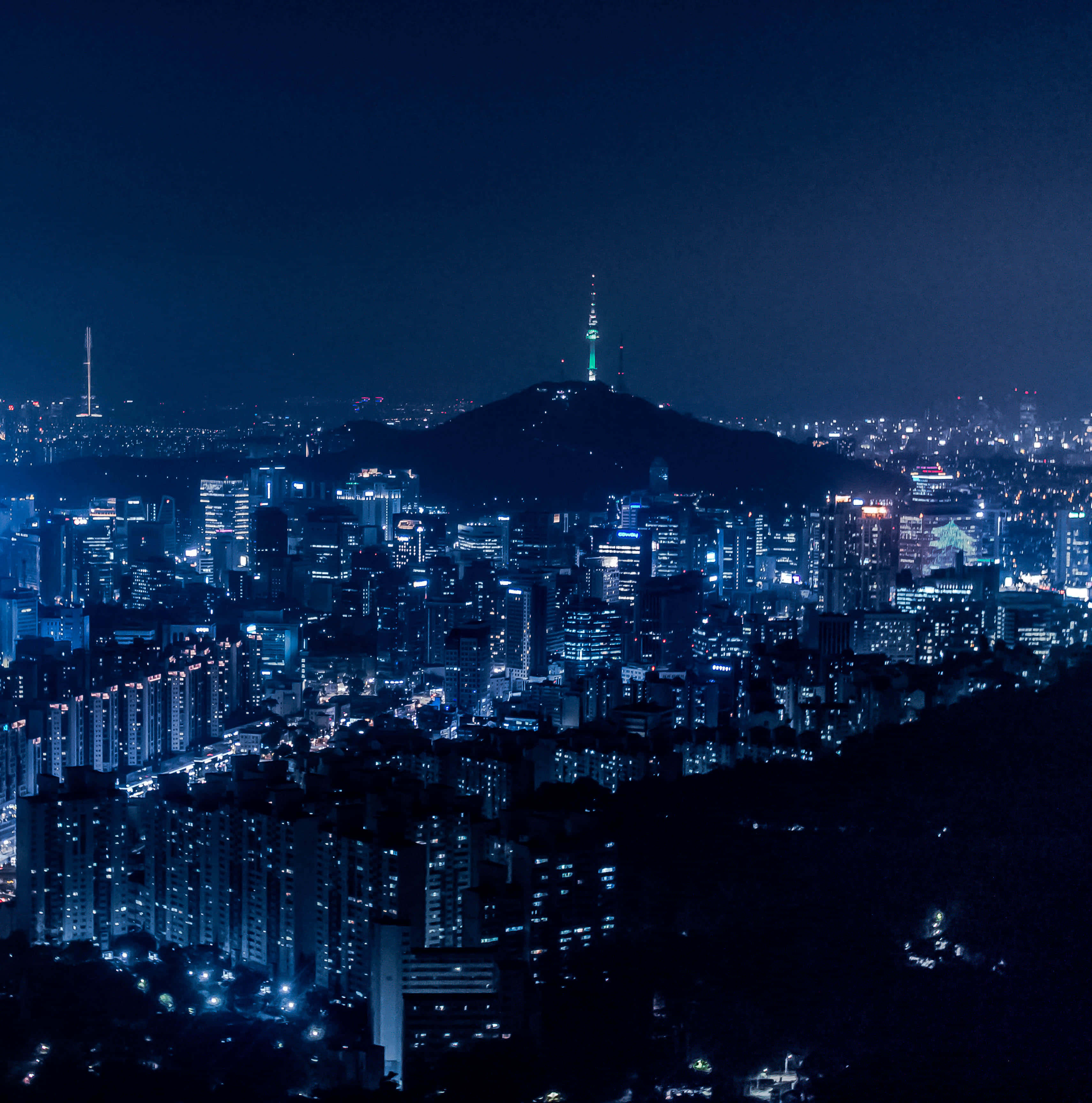 南韓 桌布 壁紙 — 廣闊的夜景城市景觀，閃爍的摩天大樓和一座山頂上點亮的塔樓，在黑暗的天空下。