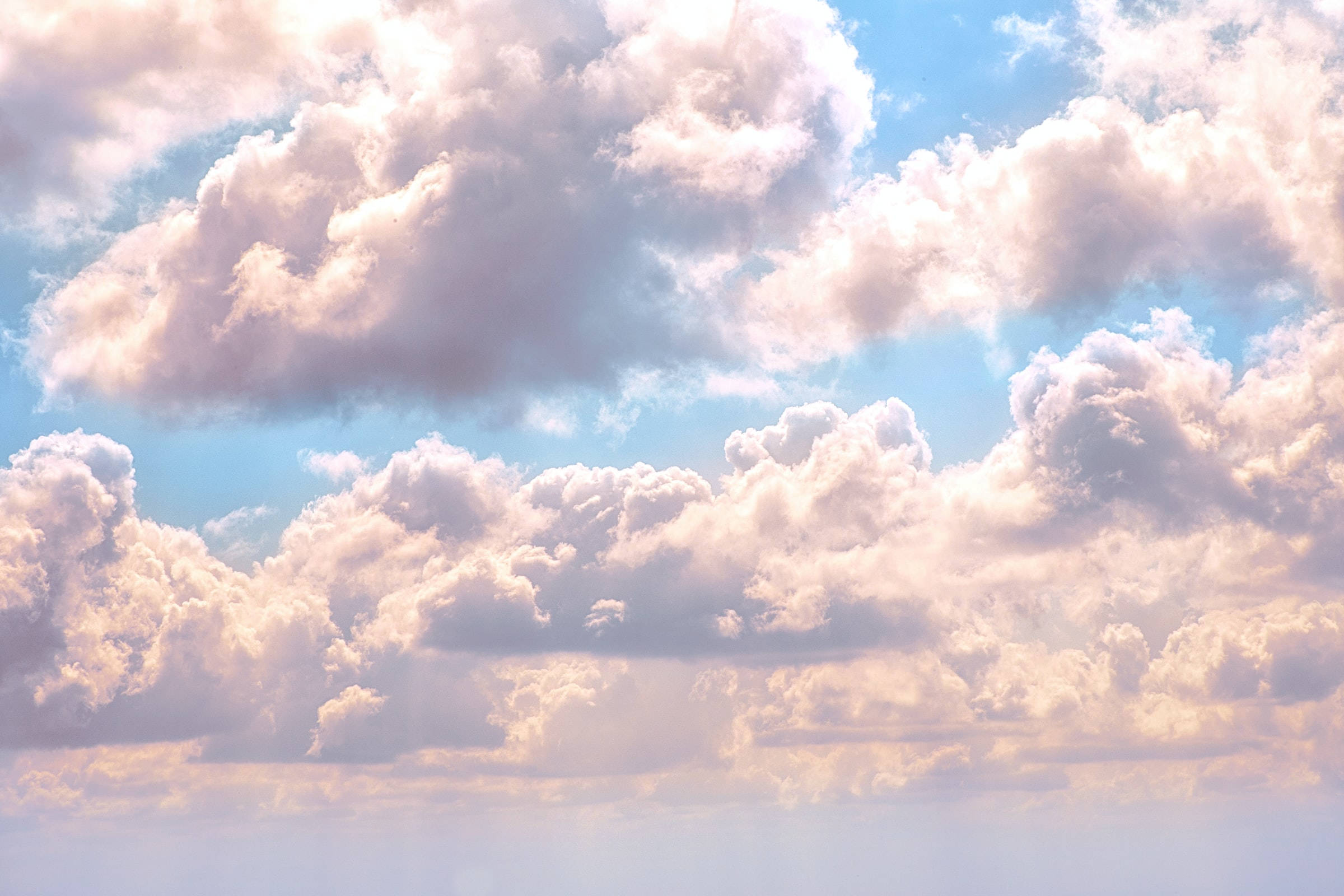 雲朵 桌布 壁紙 — 廣闊的天空充滿了蓬鬆的棉花雲，沐浴在溫暖的金色陽光下，背景是柔和的藍色。
