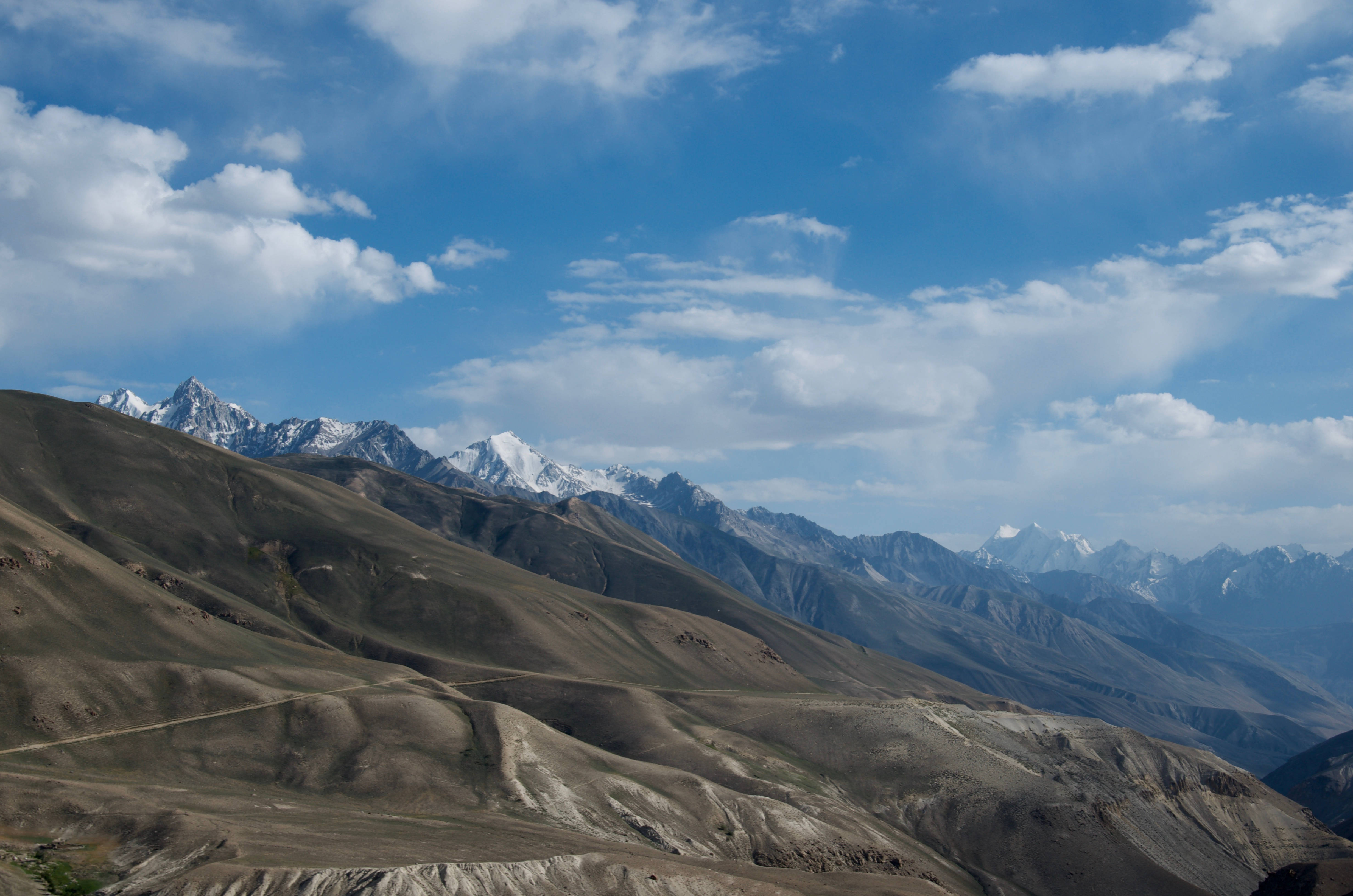Tajikistan 桌布 壁紙 — 廣闊的山脈，白雪覆蓋的山峰，在明亮的藍天下點綴著蓬鬆的白雲。