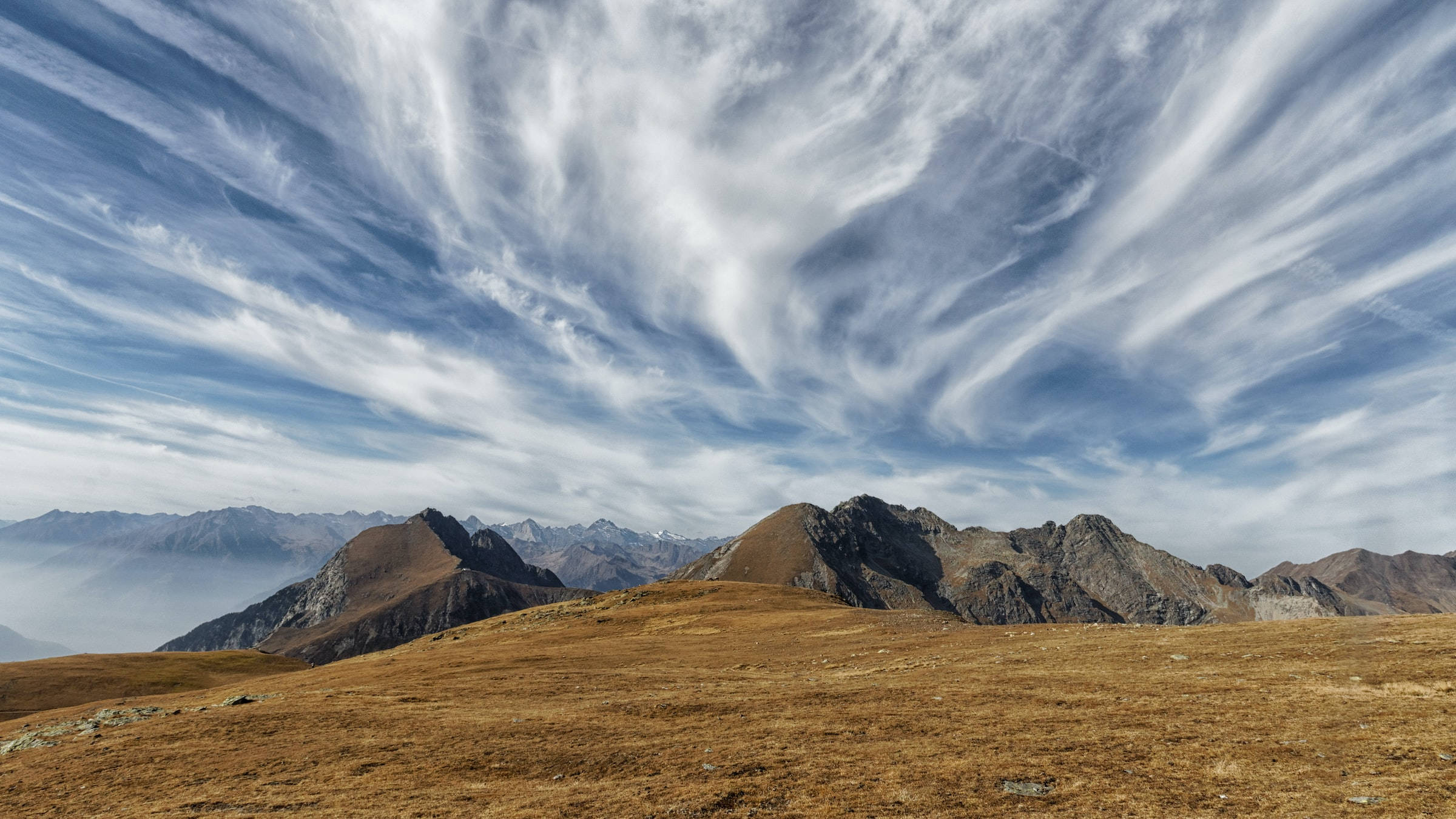 山景 桌布 壁紙 — 廣闊的山脈在充滿戲劇性漩渦雲層的天空下延伸。