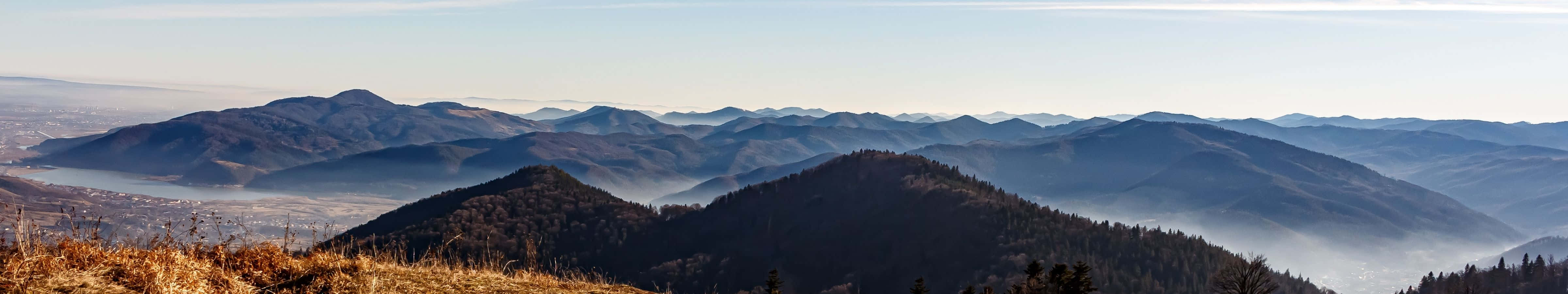 4800x900 桌布 壁紙 — 廣闊的山脈在晴朗的天空下延伸，霧氣籠罩山谷，前景是金色的草地。
