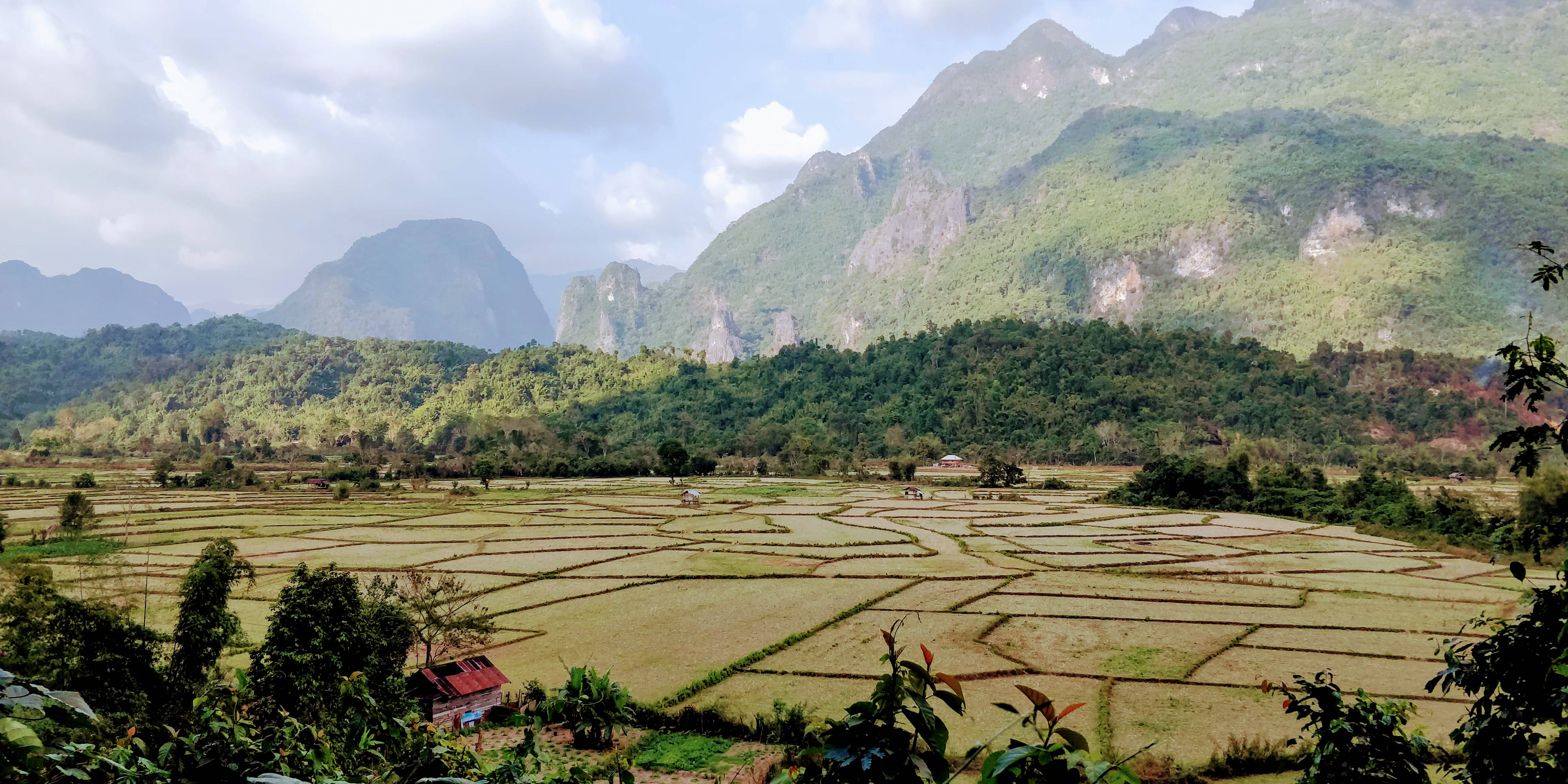 Laos 桌布 壁紙 — 廣闊的梯田在部分多雲的天空下，延伸在高聳的綠色山脈之下。