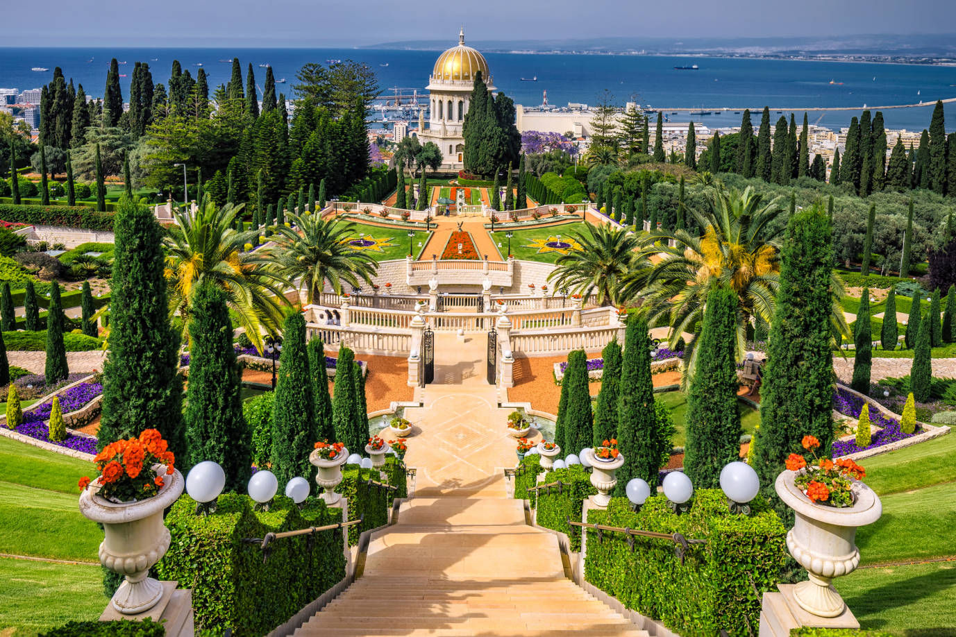 Israel 桌布 壁紙 — 廣闊的梯田花園，種有棕櫚樹和修剪整齊的樹籬，通往一座金色圓頂寺廟，俯瞰閃閃發光的藍色大海。