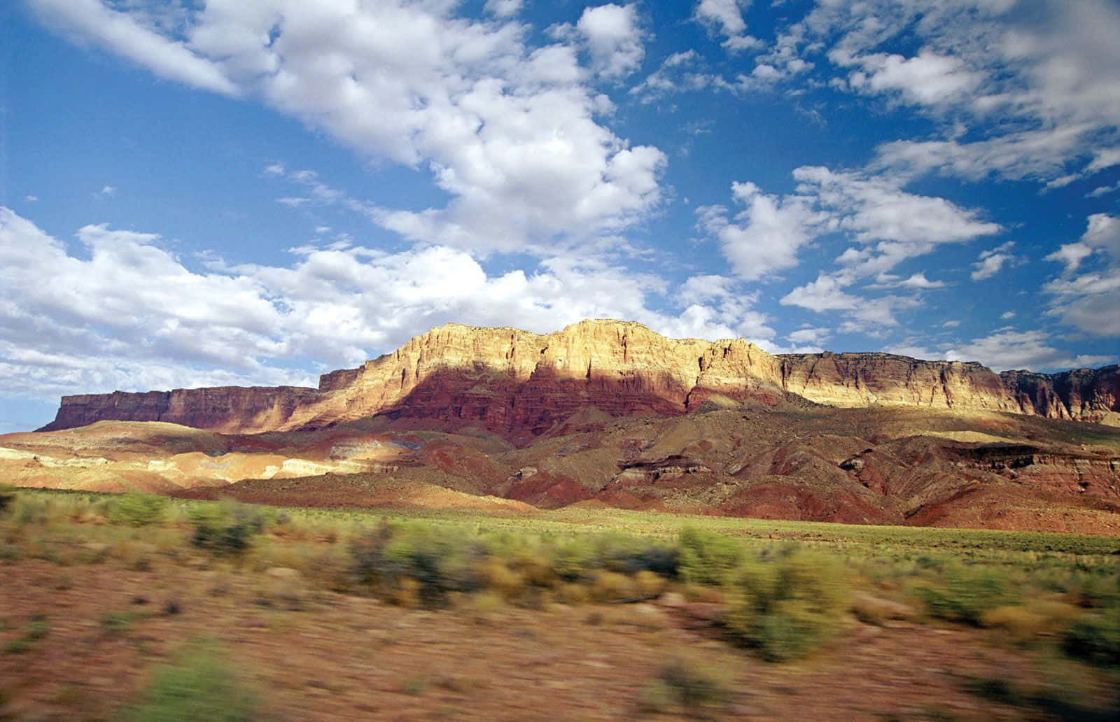 Arizona 桌布 壁紙 — 廣闊的沙漠峽谷，層層疊疊的紅色岩層，在明亮的藍天下點綴著蓬鬆的白雲。