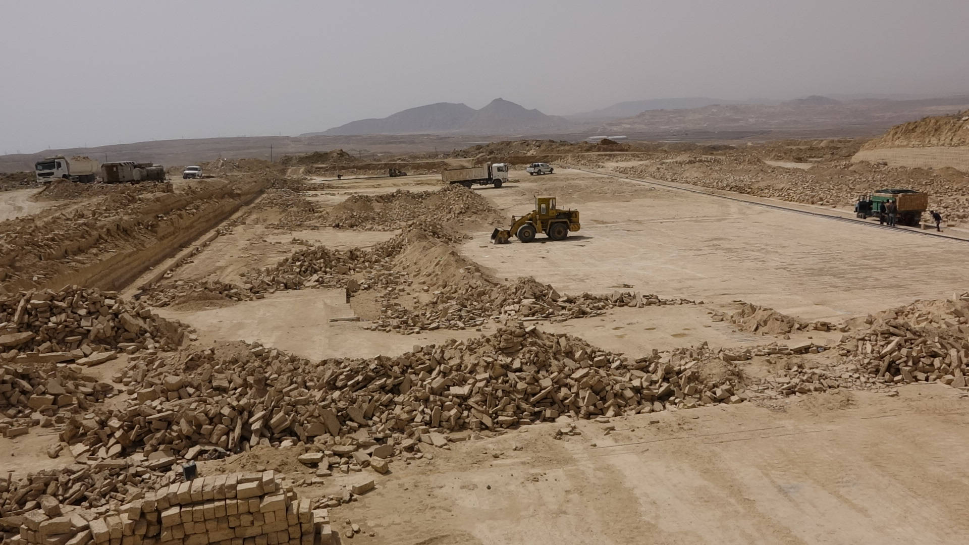 Iraq 桌布 壁紙 — 廣闊的沙漠建築工地，有瓦礫堆和黃色推土機，天空帶有薄霧。