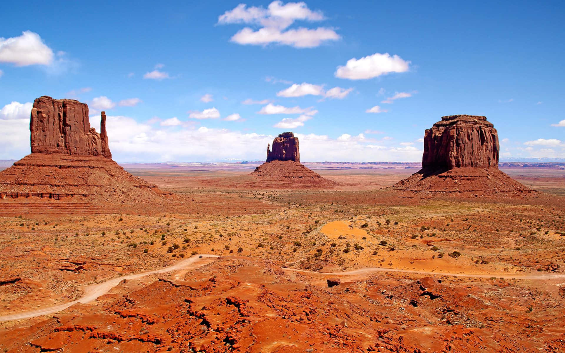 Arizona 桌布 壁紙 — 廣闊的沙漠景觀，三座標誌性的紅色岩石台地在明亮的藍天下，點綴著蓬鬆的白雲。