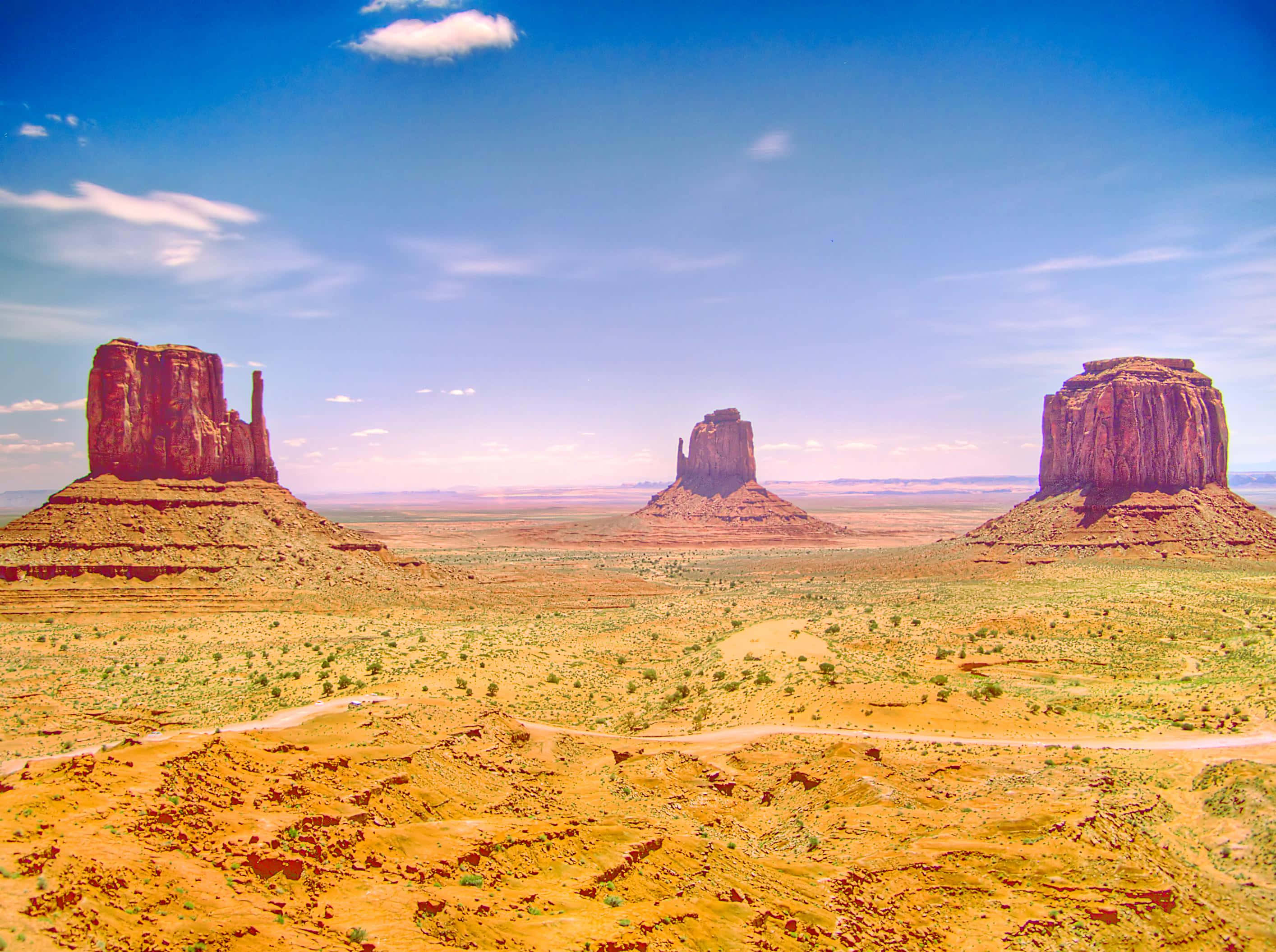 Arizona 桌布 壁紙 — 廣闊的沙漠景觀，三座標誌性的紅色岩石台地在明亮的藍天下，散佈著雲朵。