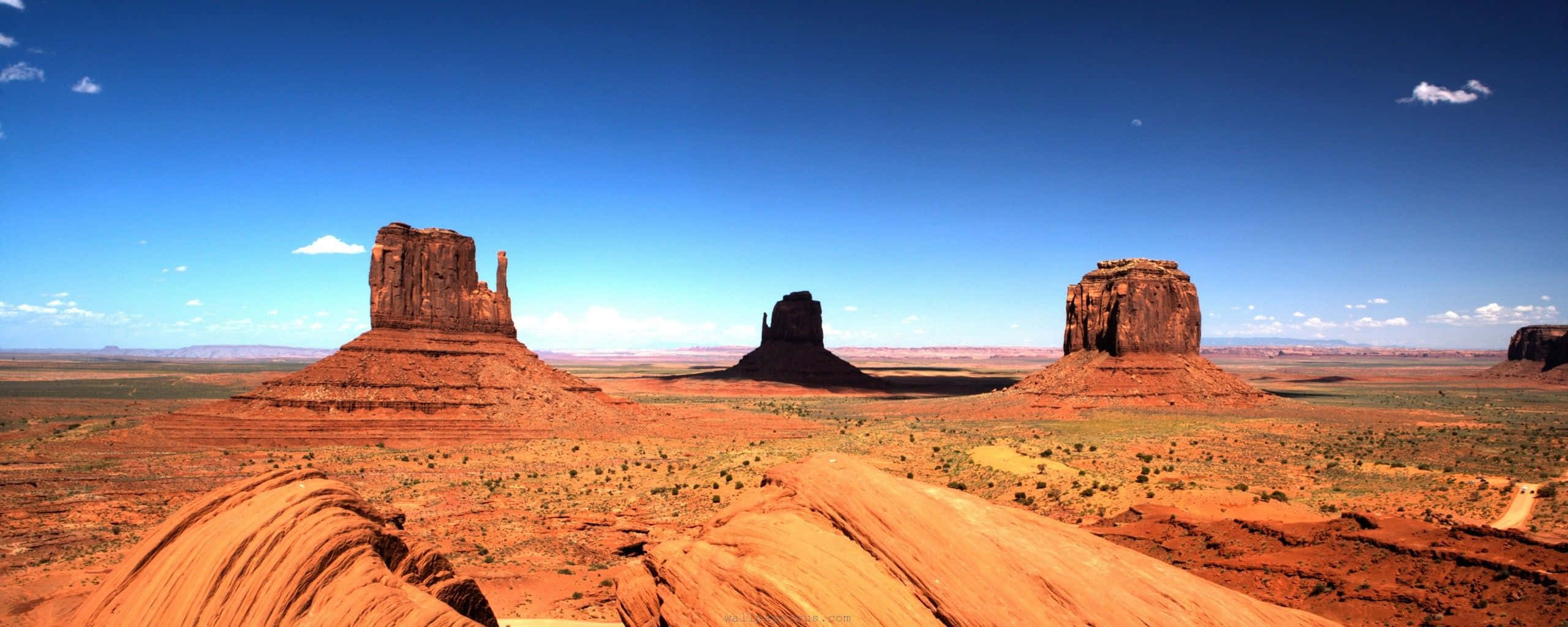 Arizona 桌布 壁紙 — 廣闊的沙漠景觀，在清澈藍天和零星雲朵下，有標誌性的紅色岩層。