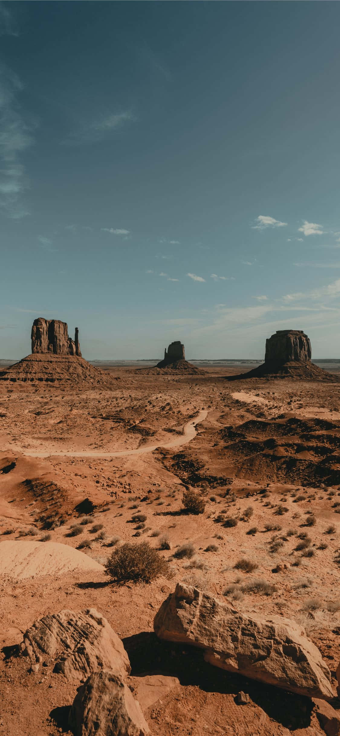 Desert iPhone 桌布 壁紙 — 廣闊的沙漠景觀，擁有標誌性的紅色岩層，在清澈的藍天和零星雲朵下。