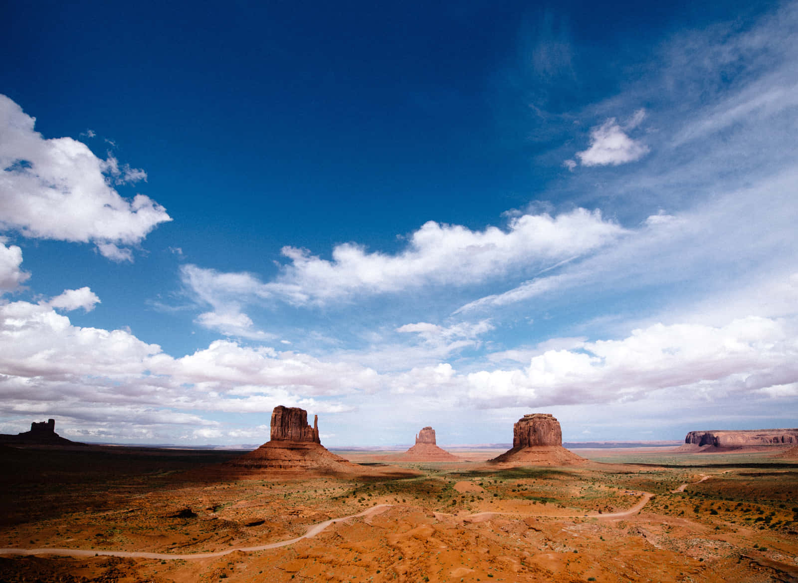 Arizona 桌布 壁紙 — 廣闊的沙漠景觀，標誌性的紅色岩石山丘在明亮的藍天下，點綴著蓬鬆的白雲。