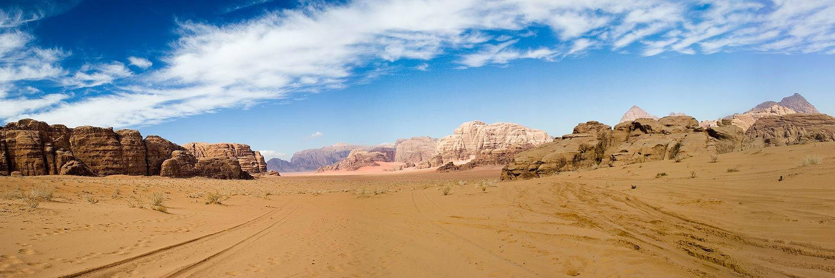 Jordan 桌布 壁紙 — 廣闊的沙漠景觀，紅色沙丘和 towering 岩石 formations 在明亮的藍天下，散佈著雲朵。