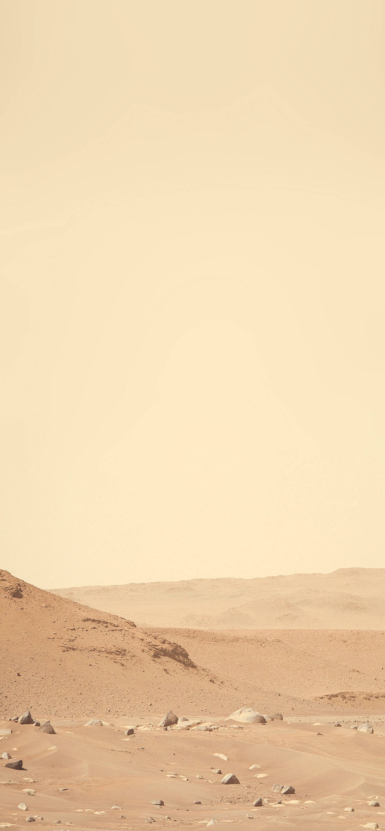 Mars iPhone 桌布 壁紙 — 廣闊的沙漠景觀，連綿起伏的沙丘和散落的岩石，籠罩在朦朧的橙色天空下。