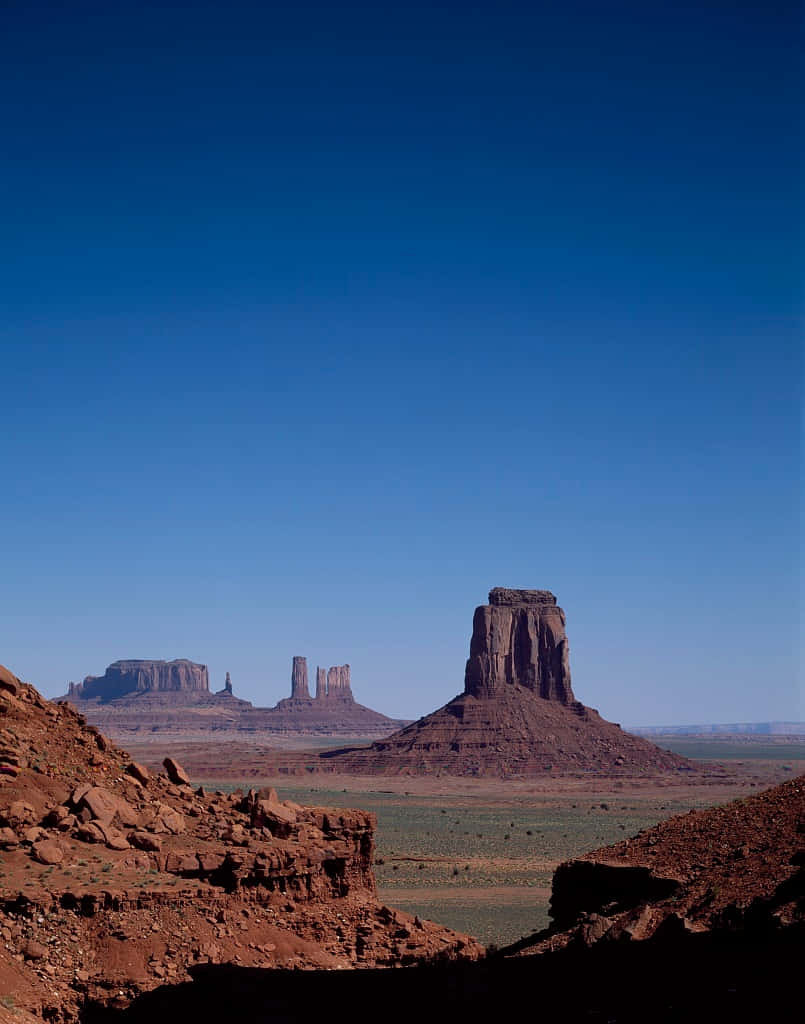 Arizona 桌布 壁紙 — 廣闊的沙漠景觀，高聳的紅色岩石孤峰在清澈深藍的天空下。