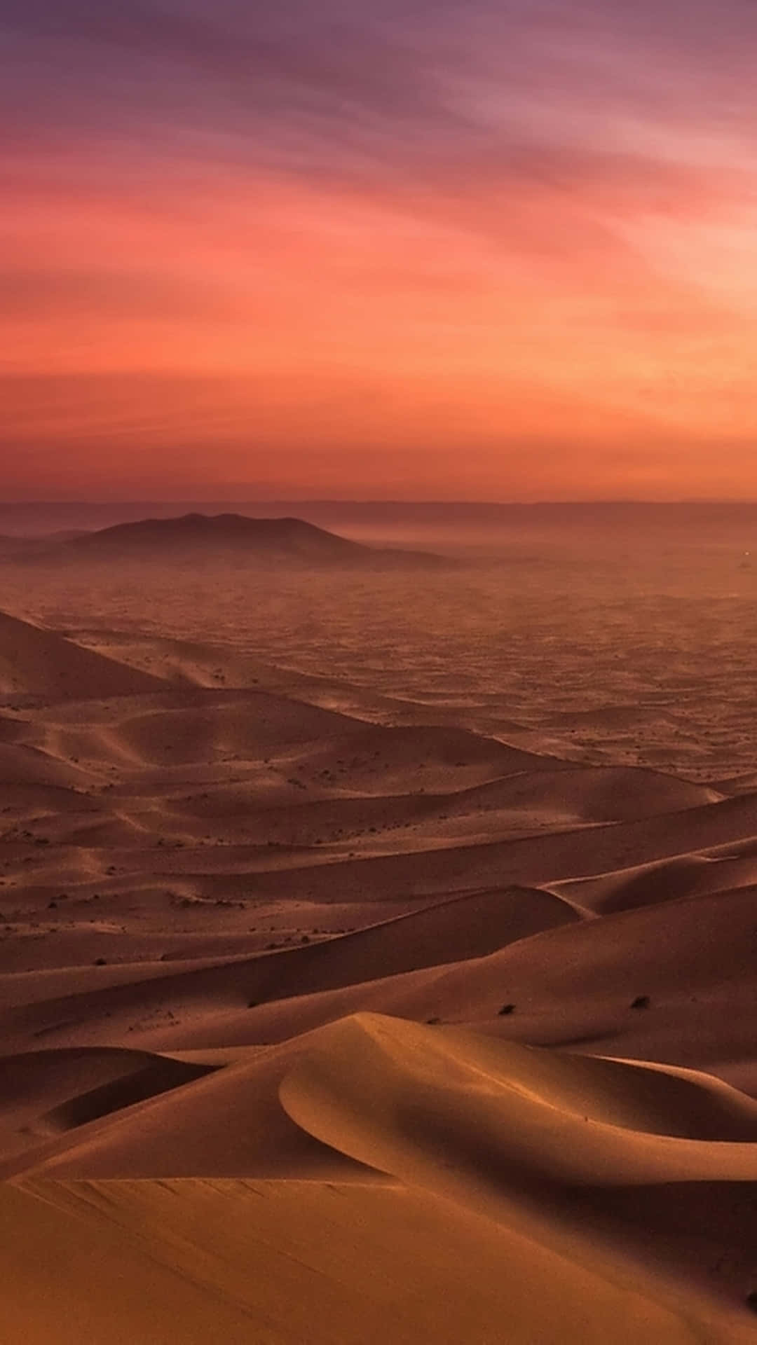 Desert iPhone 桌布 壁紙 — 廣闊的沙漠景觀在日落時分，起伏的沙丘在漸變的天空下沐浴在溫暖的橙色和粉紅色調中。
