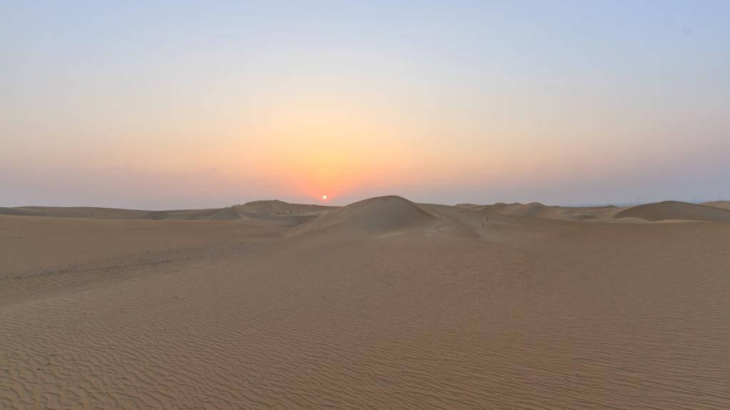 Desert Sun 桌布 壁紙 — 廣闊的沙漠景觀在日落時分，金色沙丘延伸向發光的地平線。