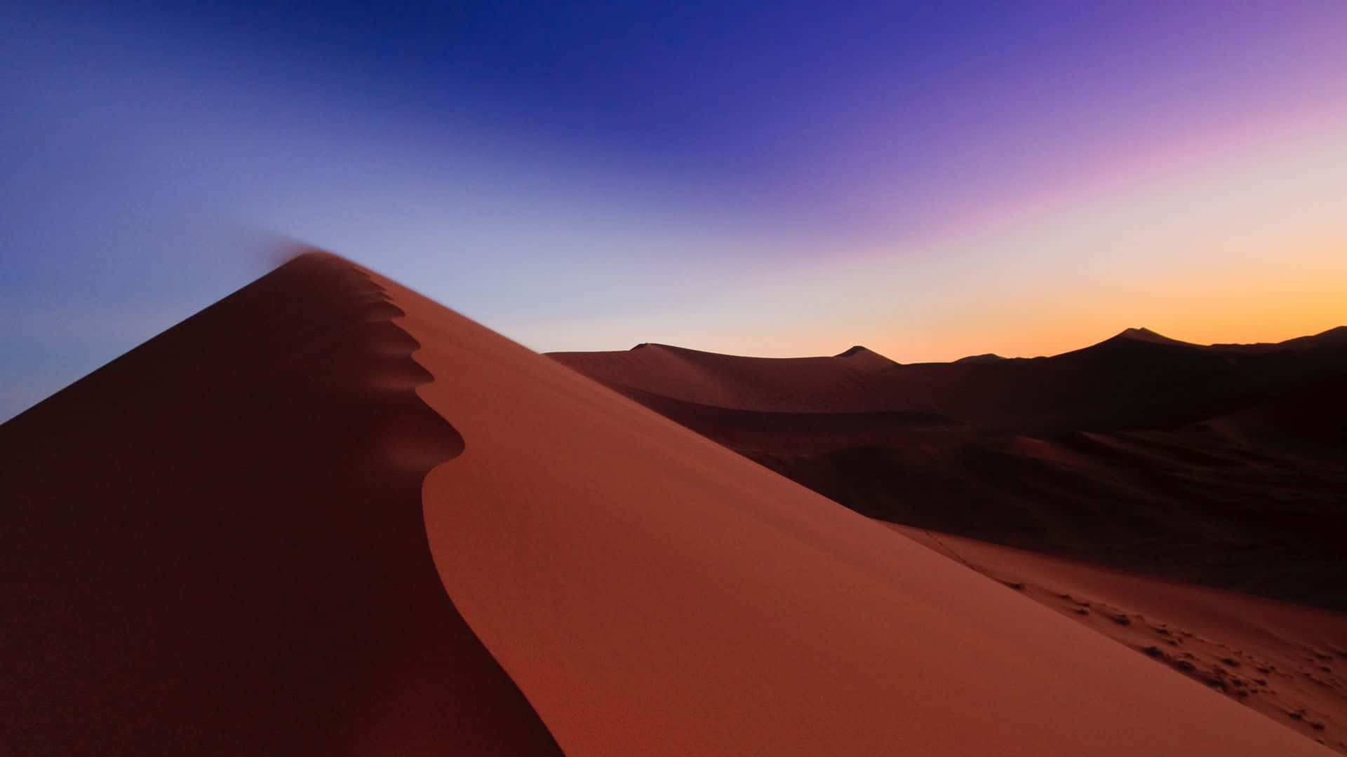 Sand Dunes 桌布 壁紙 — 廣闊的沙漠沙丘景觀，沐浴在紫色、橙色和深藍色的暮色中，帶有柔和的風吹沙紋理。