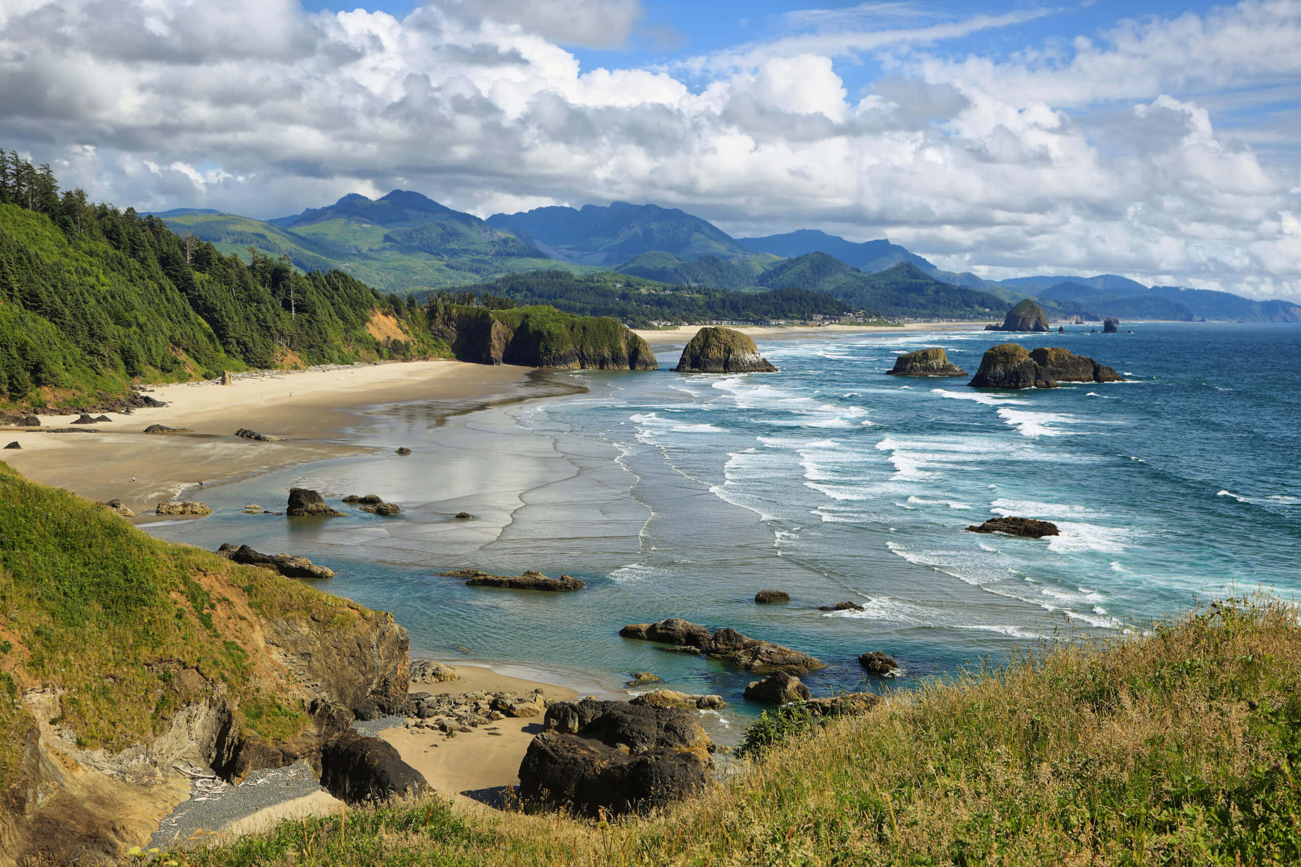Oregon Coast 桌布 壁紙 — 廣闊的海岸景觀，在部分多雲的天空下，碧綠色的波浪拍打著岩石海岸。
