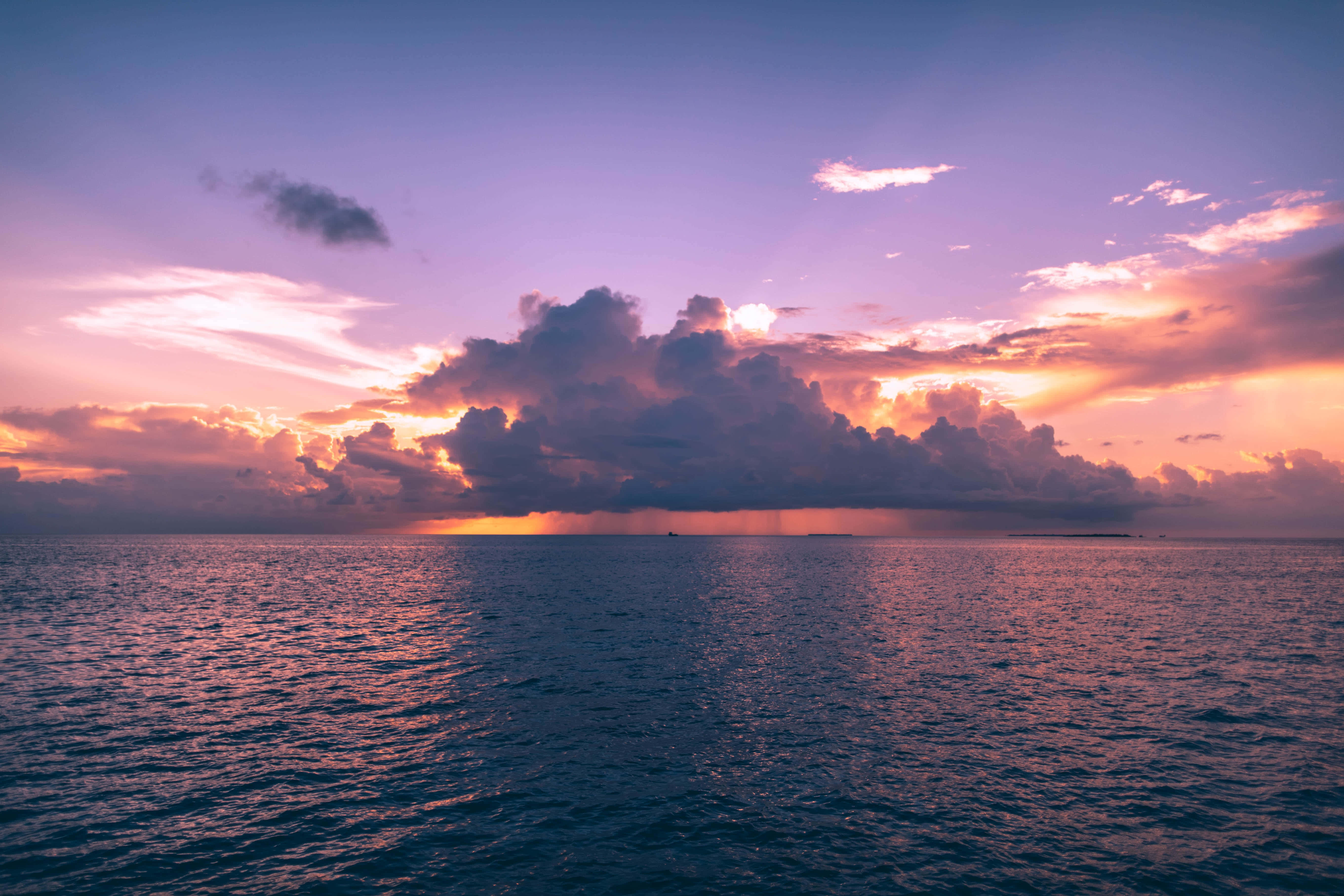 風景 桌布 壁紙 — 廣闊的海洋在日落時分，戲劇性的紫色和橙色雲彩倒映在漣漪的水面上。