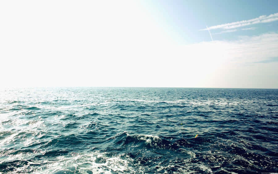 Aesthetic Tumblr Desktop 桌布 壁紙 — 廣闊的海洋波浪在明亮的陽光下蕩漾，一道淡淡的凝結尾跡劃過淡藍色的天空。